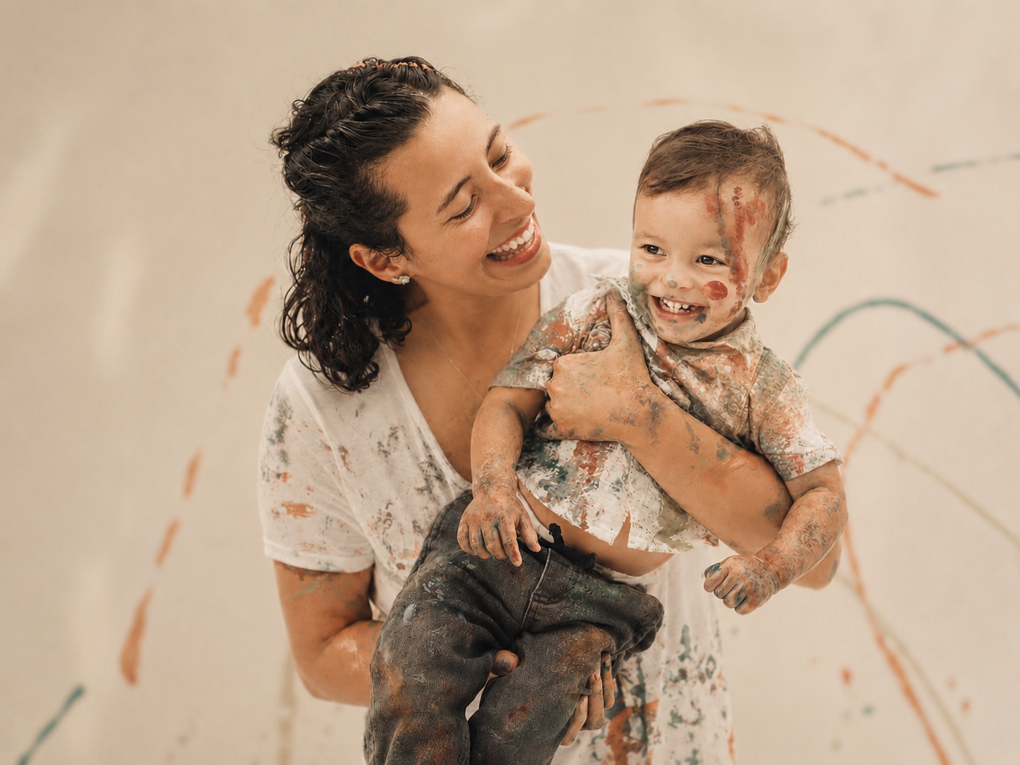 A woman and a young boy covered in colorful paint, smiling and enjoying a playful moment together.