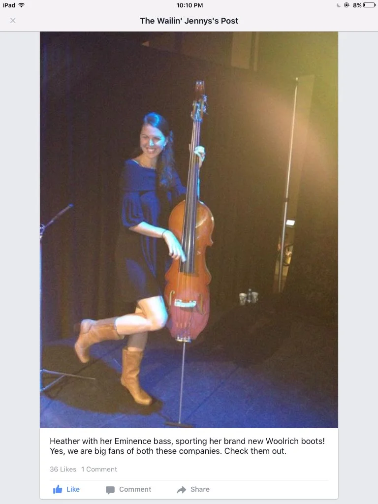 A woman wearing a blue dress and tan boots posing with a double bass on stage.