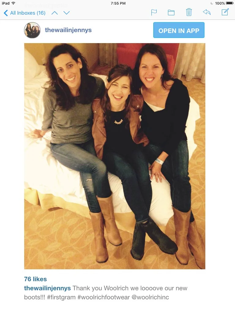 Three women sitting on a bed, smiling and posing for a photo, all wearing boots and casual clothing.