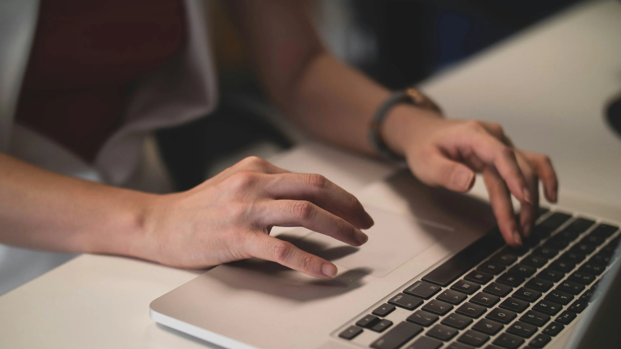 Close-up of hands typing on a laptop keyboard, with a person in the background.