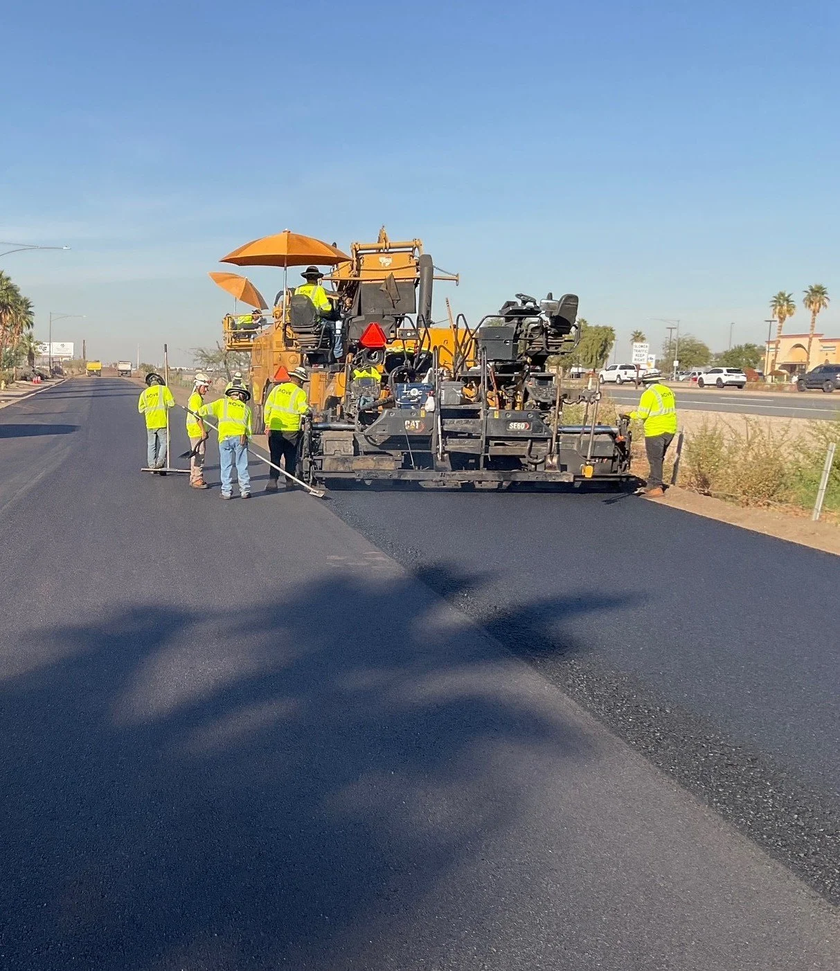 Workers paving a road with asphalt using heavy machinery under a clear blue sky.