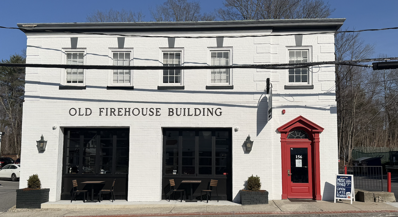 Exterior of Wogies Katonah in a white brick former firehouse with a red entrance door.