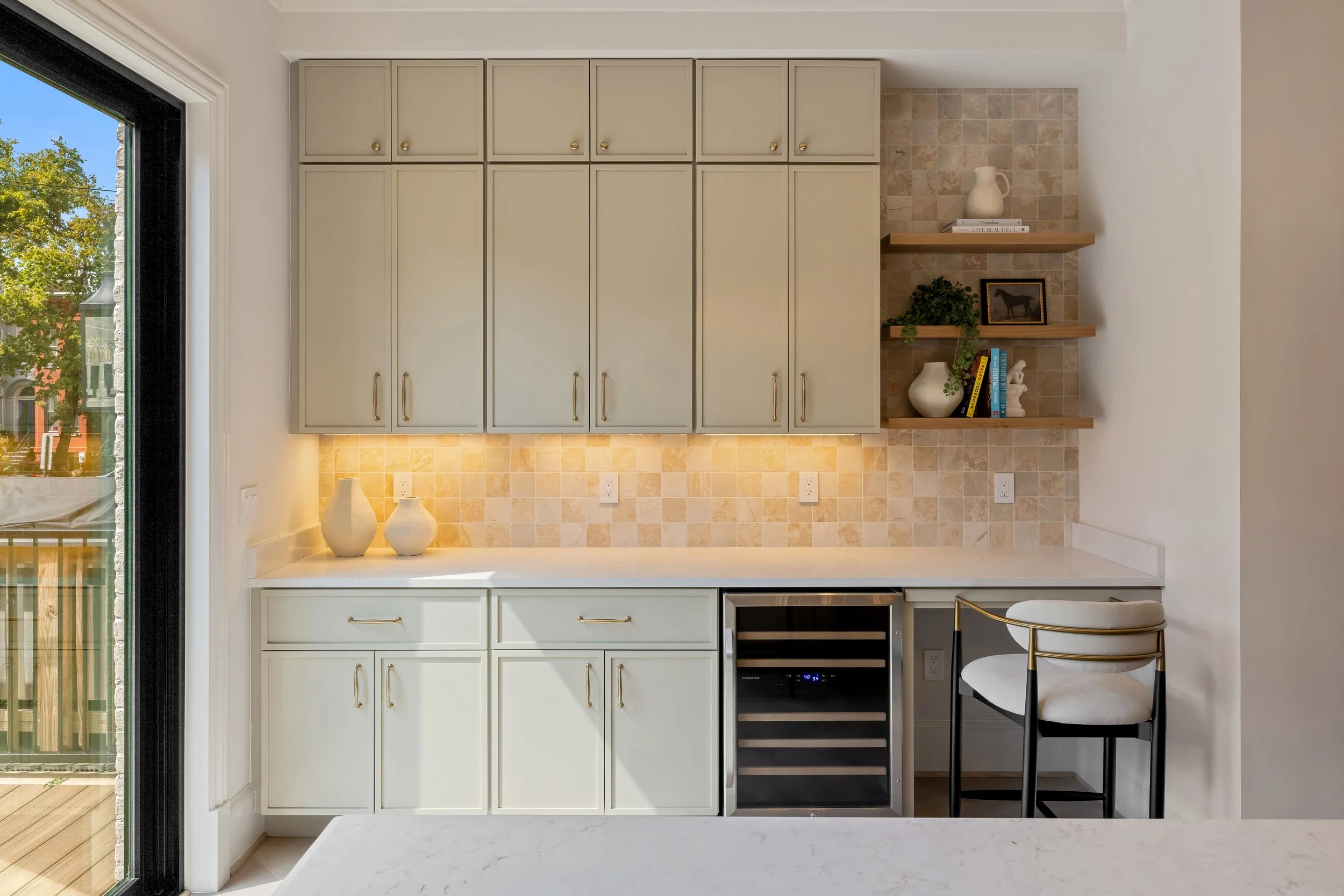 Open-concept modern kitchen with a large island featuring barstools, dark wood cabinetry, built-in shelves, and a stylish chandelier overhead in a bright and airy living space.