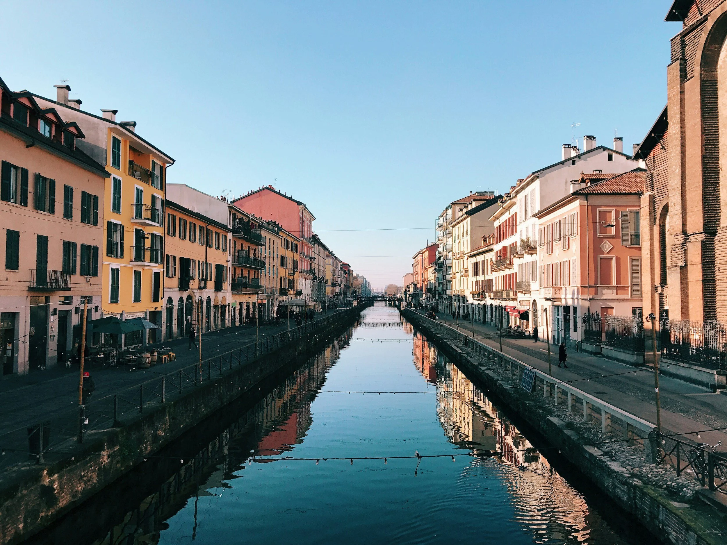 A canal with calm water reflecting colorful apartment buildings on either side under a clear blue sky.