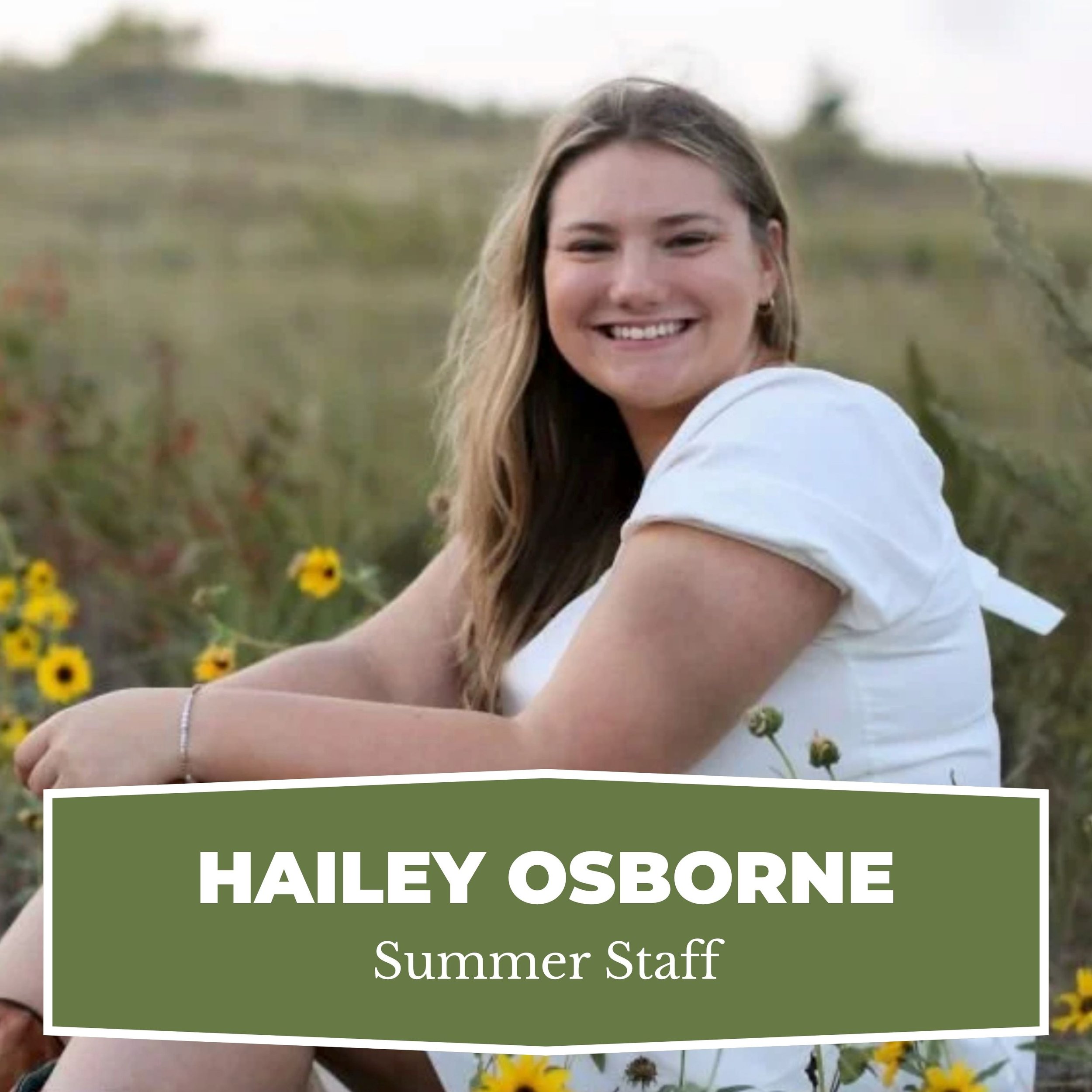 A young woman with long, wavy hair smiling while sitting in a field of yellow flowers.