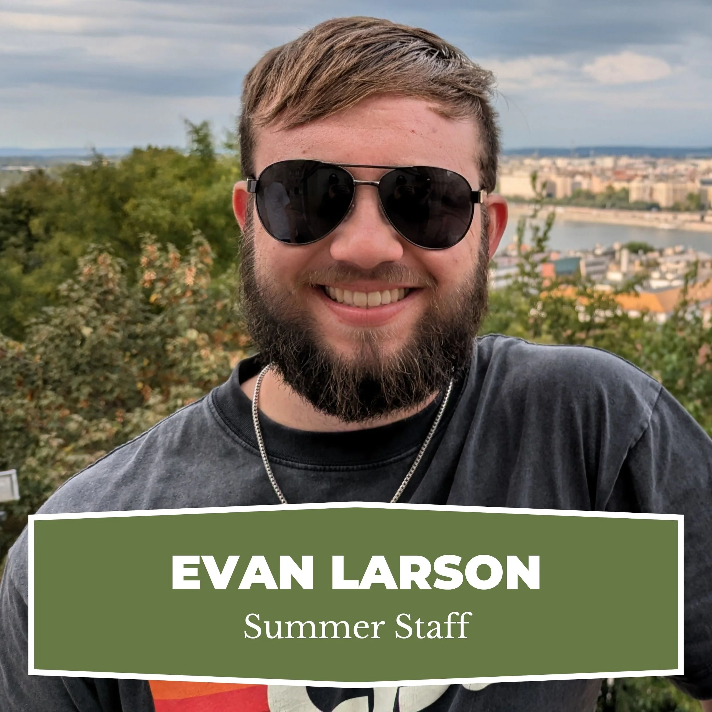Smiling man wearing sunglasses outdoors with cityscape and river in the background, labeled 'Evan Larson Summer Staff'.