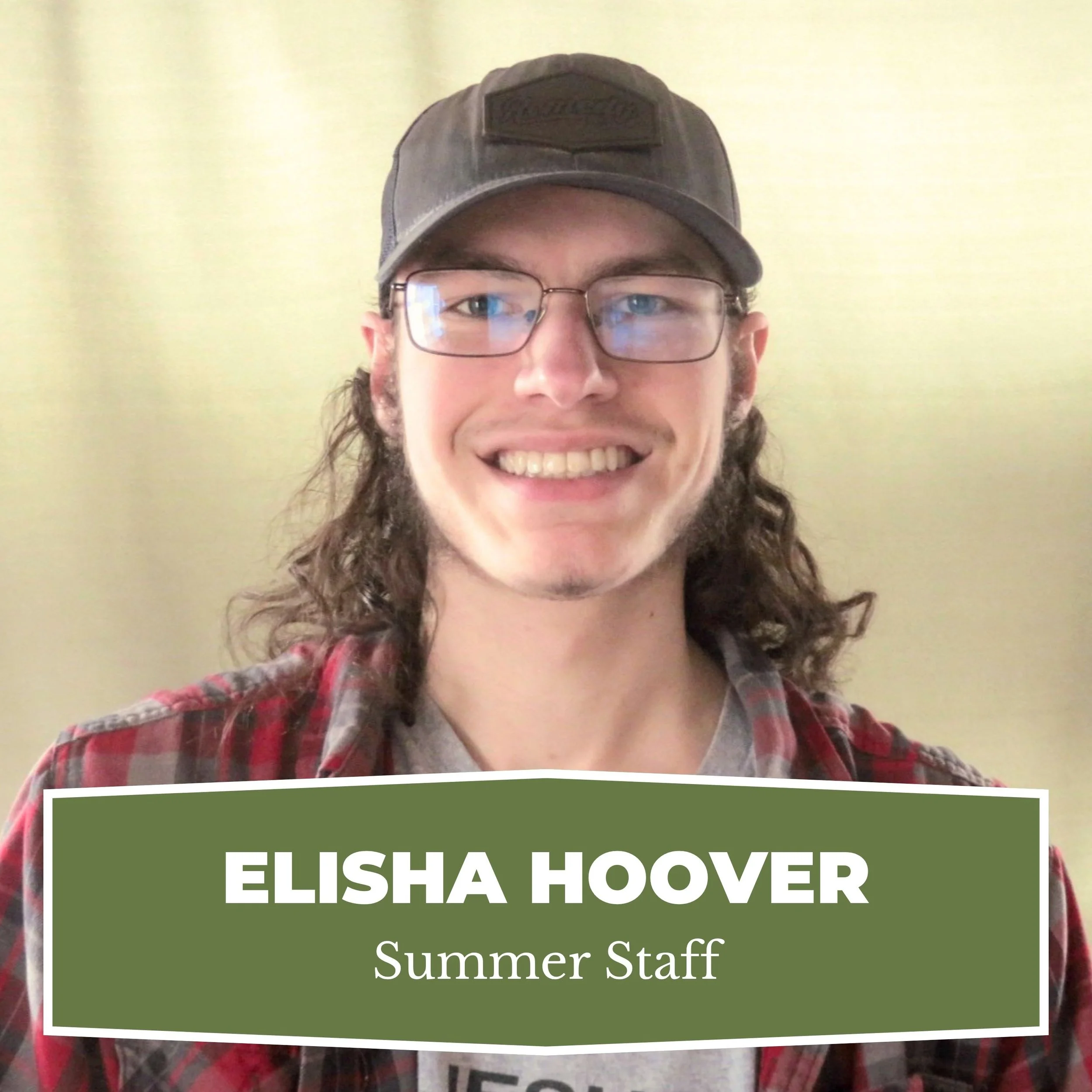 A young man with long curly hair, glasses, and a gray cap smiles at the camera. He is wearing a red plaid shirt over a light-colored T-shirt. There is a green name tag overlay that reads "Elisha Hoover, Summer Staff."