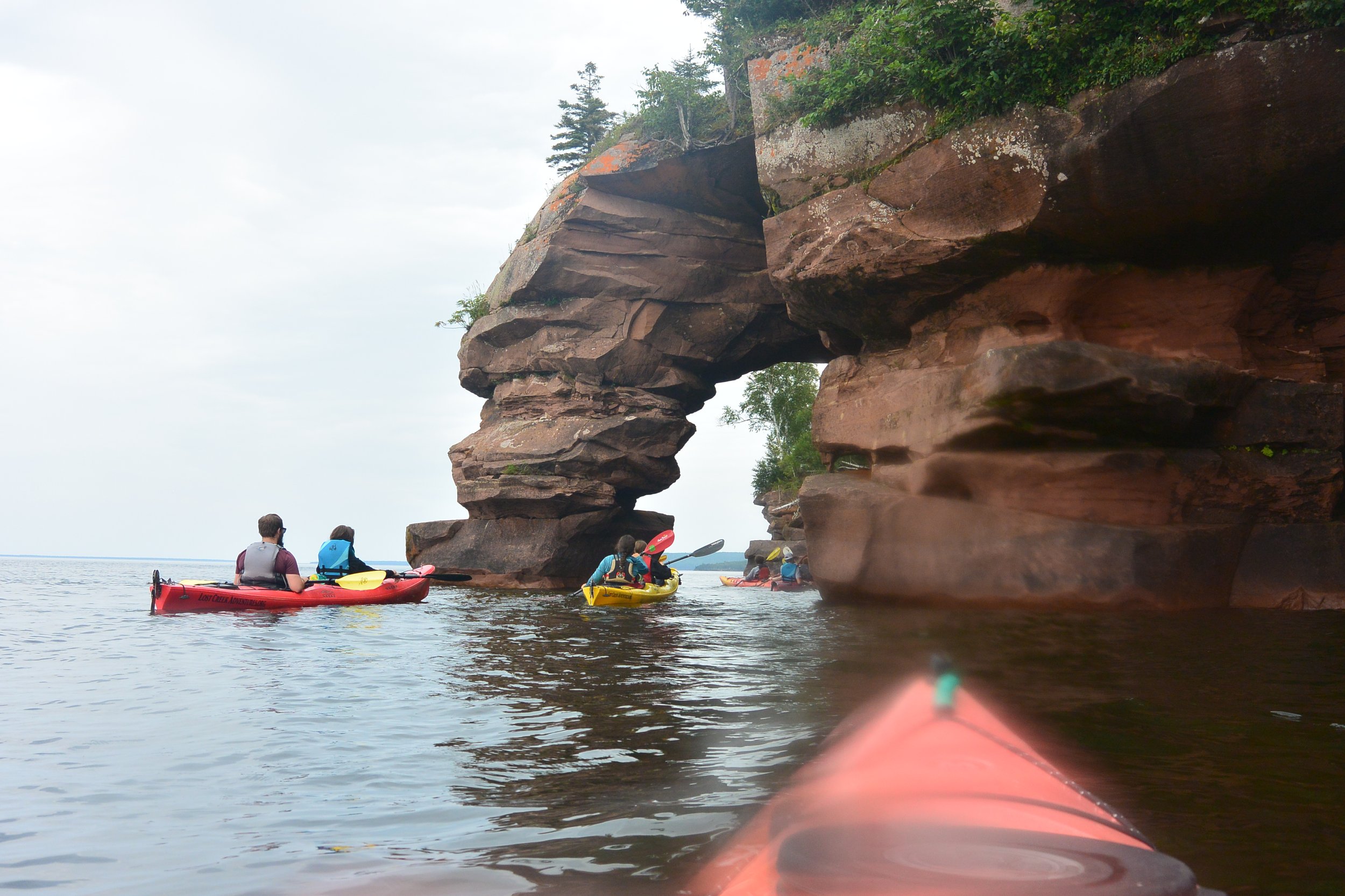 Group of people kayaking near a large rock formation with a natural arch on a body of water.