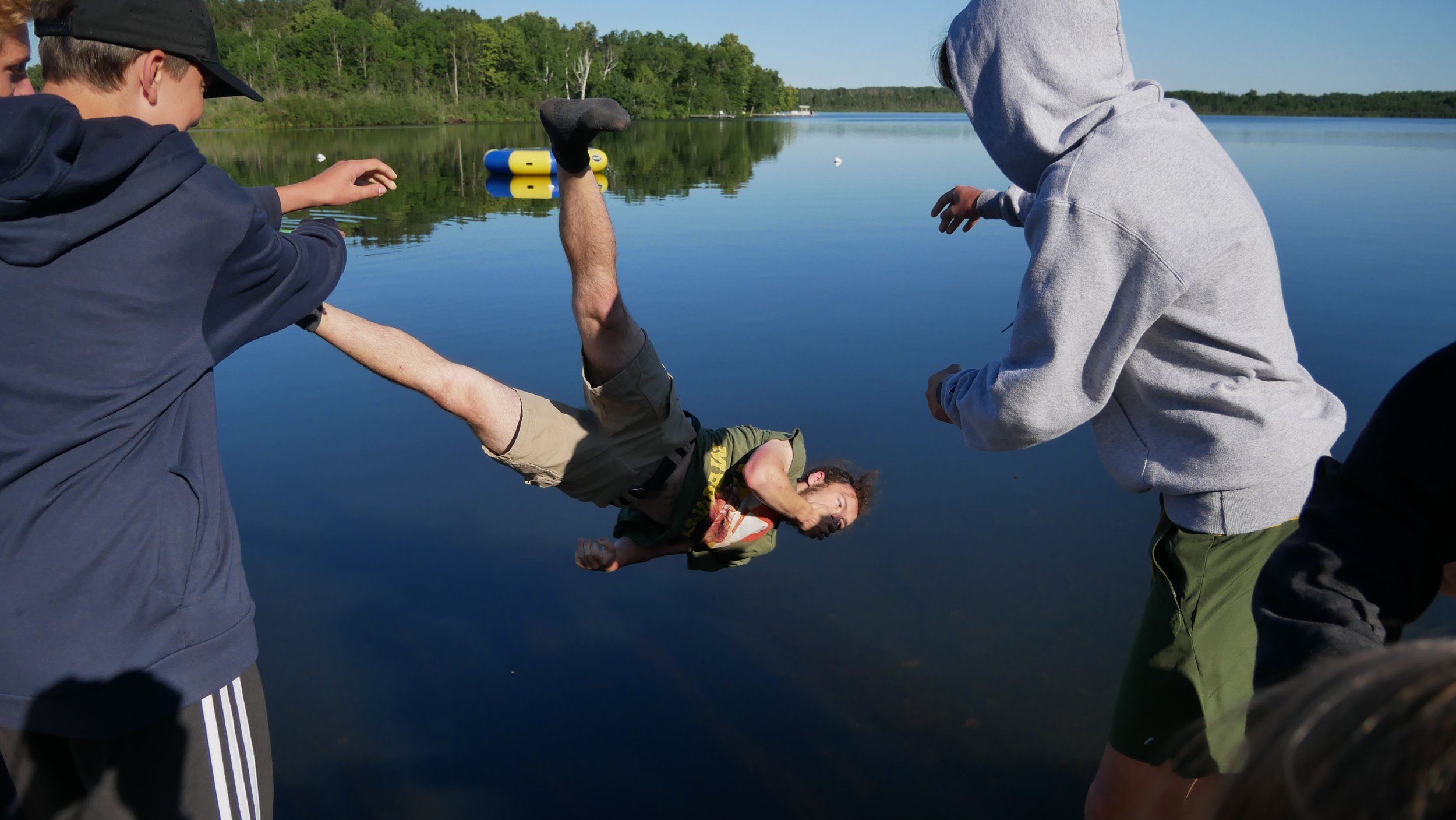 A man being pushed into a lake by several people on a sunny day.