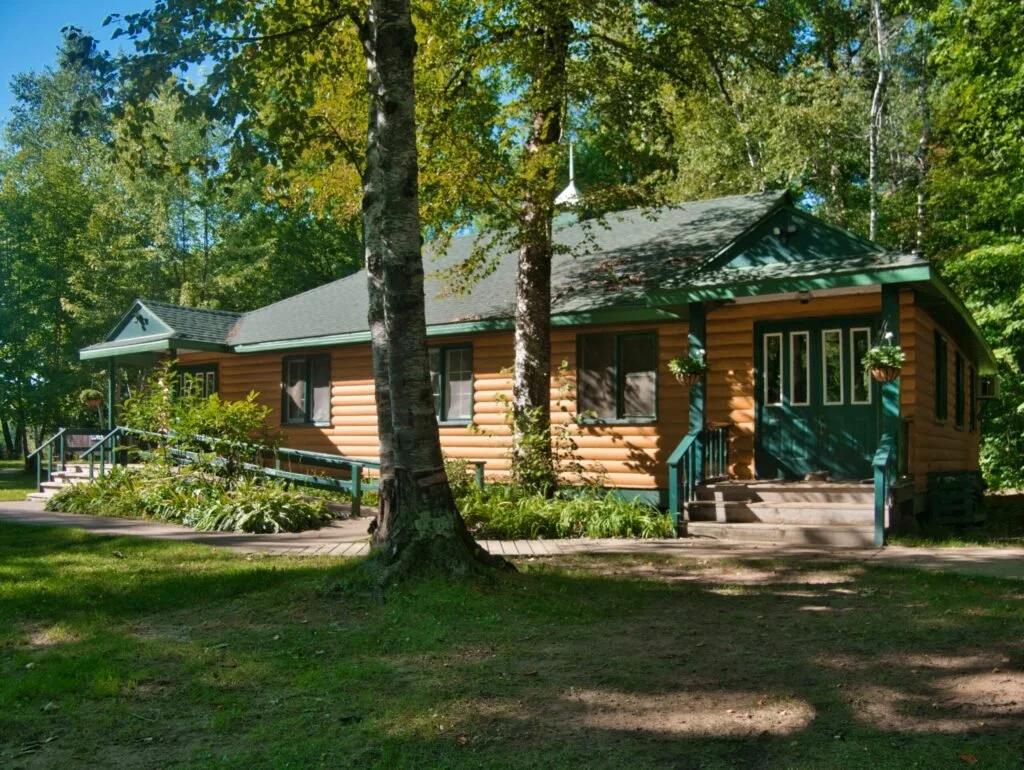 A cozy wooden house surrounded by lush green trees and a well-kept lawn.