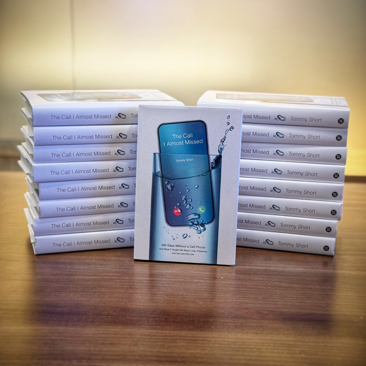 Stack of books titled 'The Call I Almost Missed' by Tommy Short, with a single copy in front displaying the same title and cover art of a smartphone with water splashing.