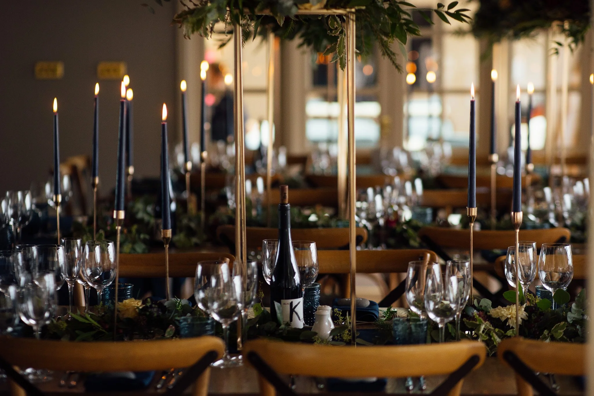 A decorated indoor dining setup with high black candles, wine glasses, and greenery, possibly for a special event or celebration.