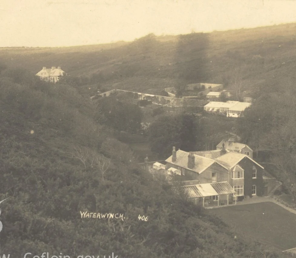 A black and white photo of a hillside with several houses scattered across the landscape, including a large house in the foreground and more houses further up the hill, labeled 'Waterwynch 406'.