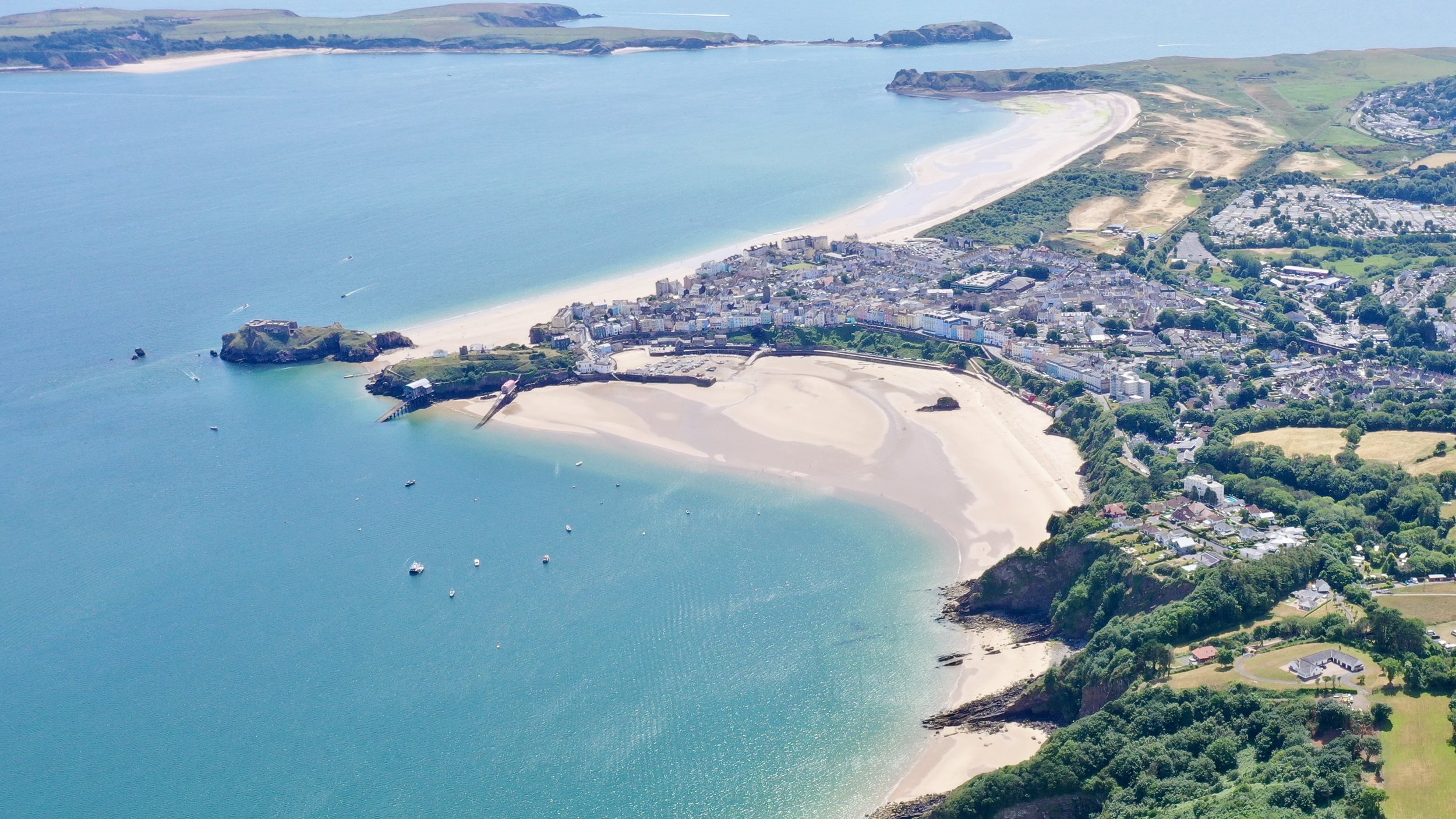 Aerial view of a coastal town with beaches, boats, and green hills.