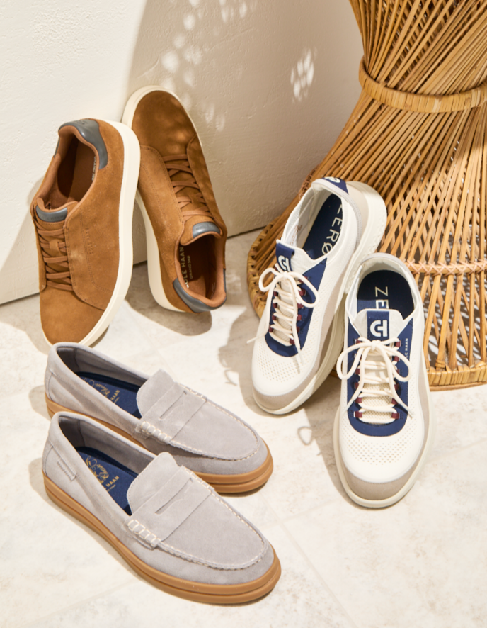 Brown slip-on shoes, white and navy sneakers, and gray suede loafers arranged beside a wicker chair
