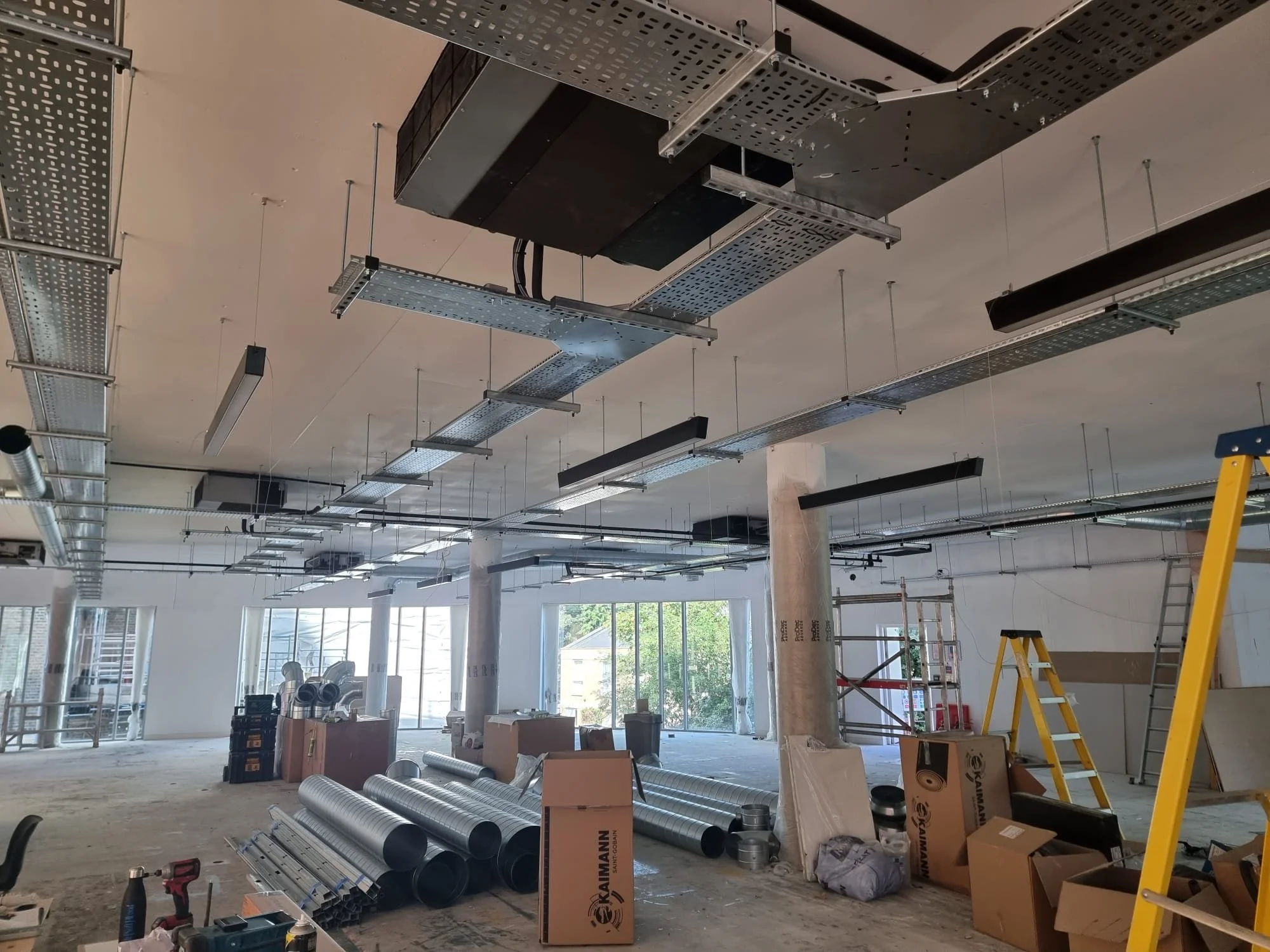Construction site with exposed ceiling, scaffolding, ladders, and construction supplies in a building under renovation or construction.