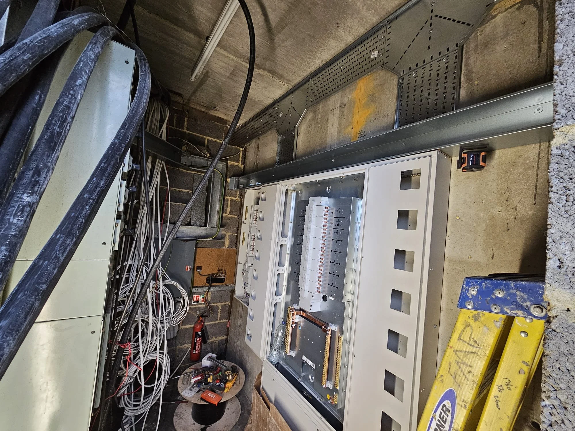 Electrical panel and wiring installation in a basement or utility room with tools and equipment.