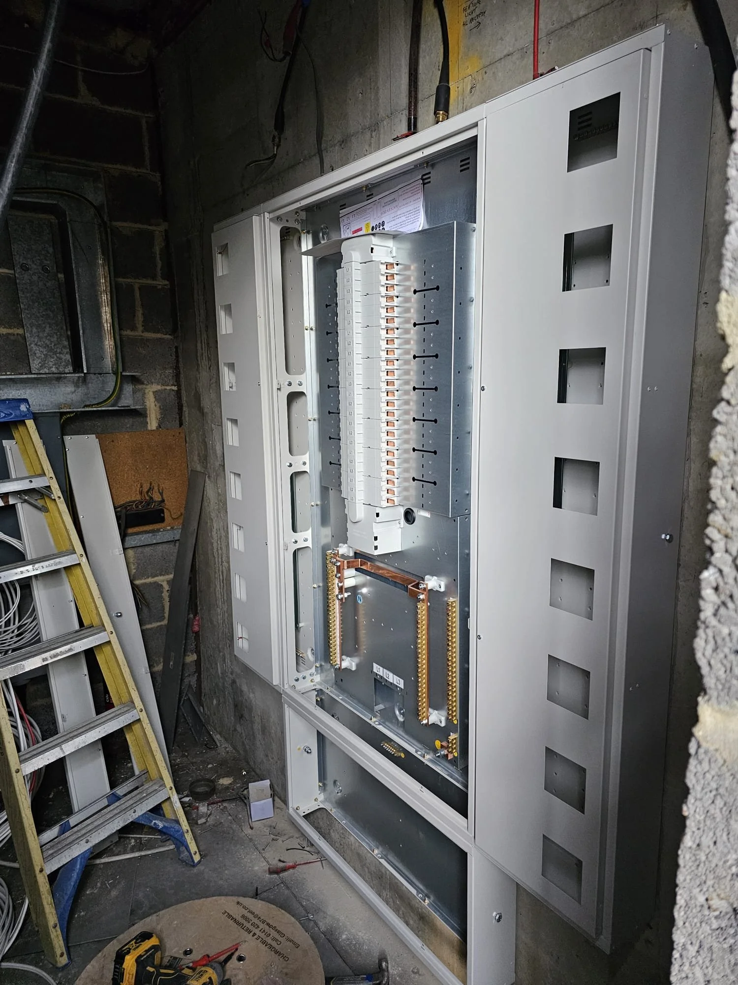 Close-up view of an electrical panel under installation in a building in a construction area, with tools and construction materials around.