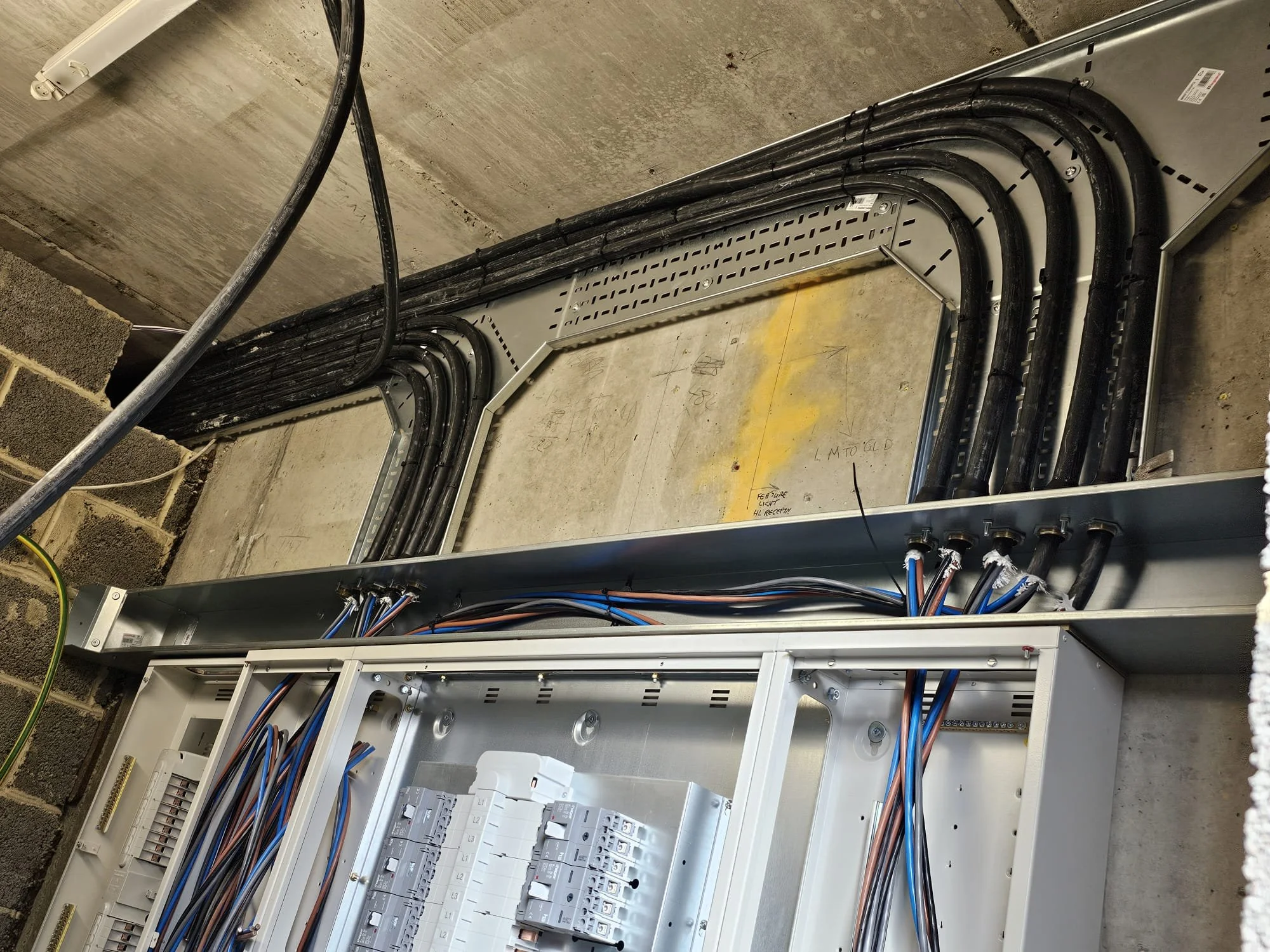 Electrical wiring and conduit installation inside an unfinished building with visible electrical panels and conduit pathways.