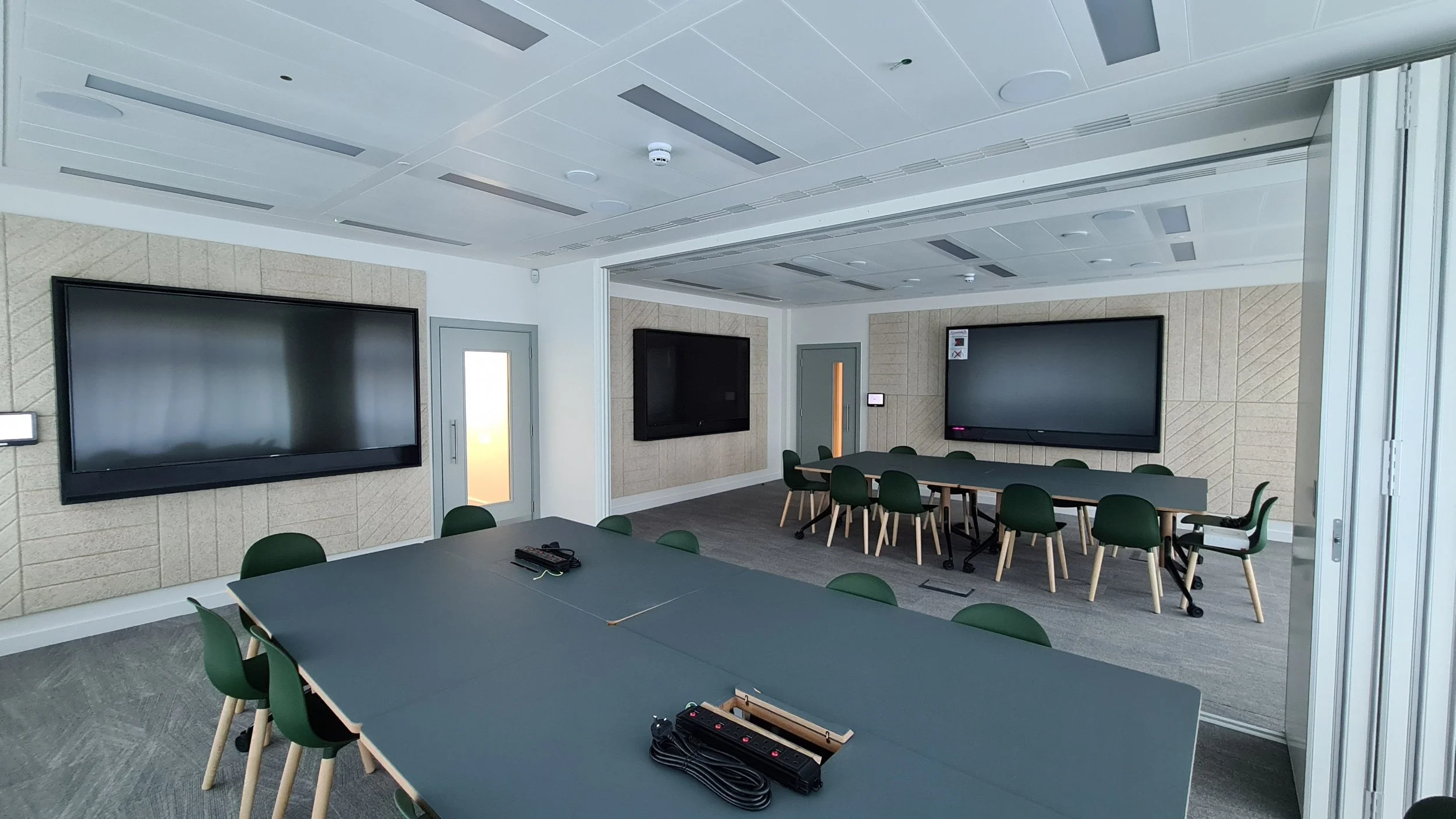 Modern conference room with large TV screens, a central table with chairs, and a smaller table, set up for meetings or presentations