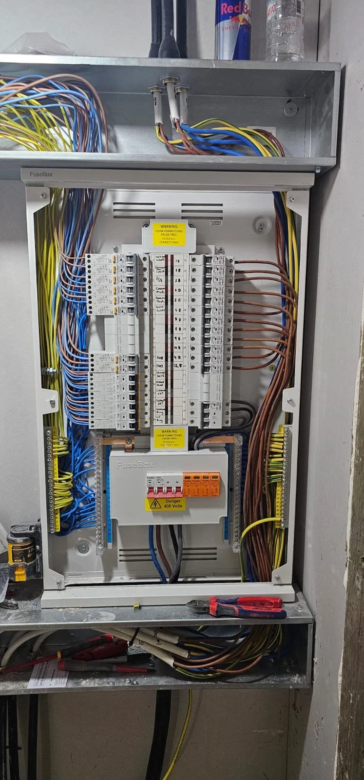 Electrical circuit breaker panel with various switches, wiring, and warning labels, some tools are placed on the metal shelf.