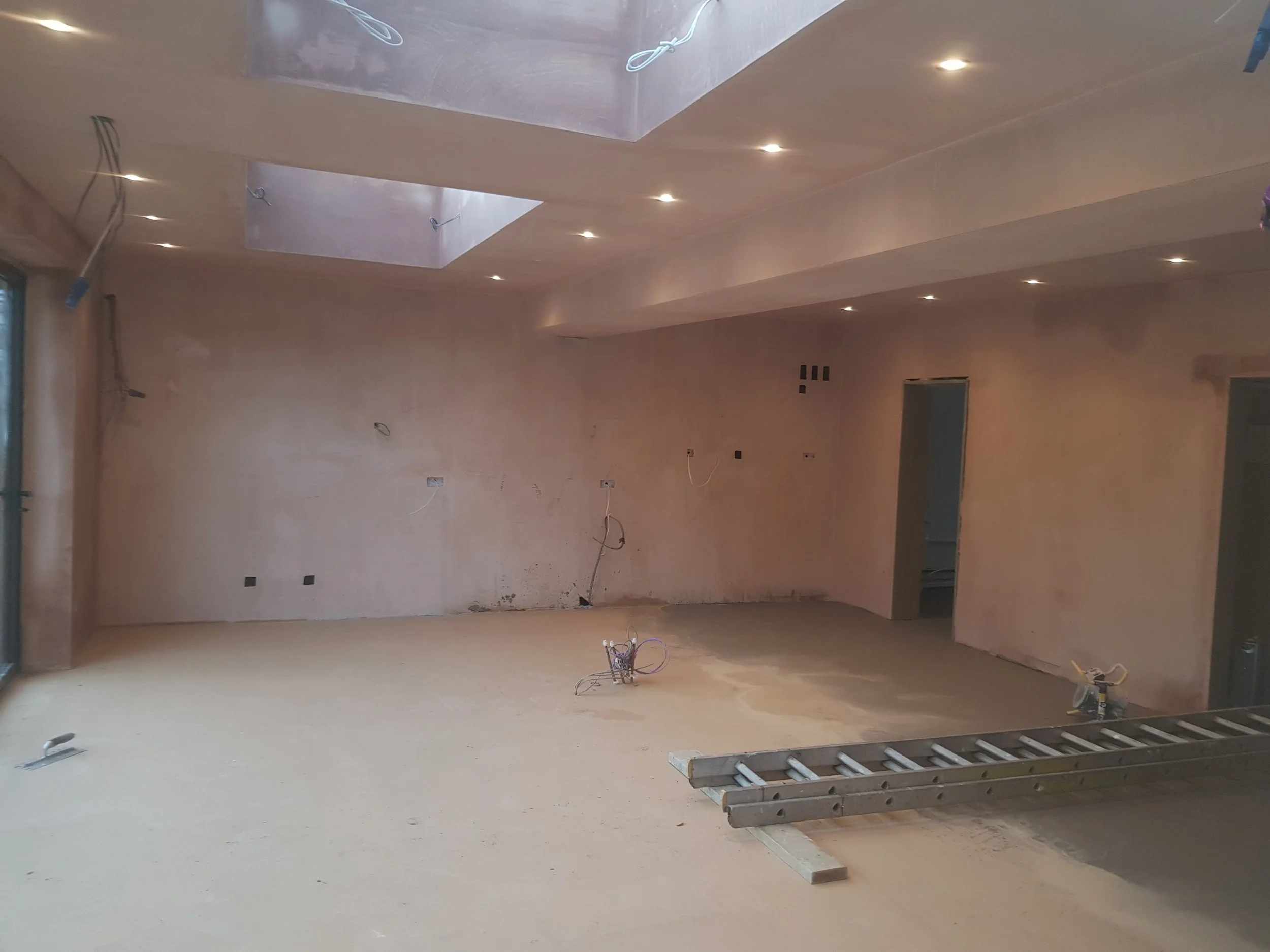 An unfinished interior room under construction with exposed wiring, a ladder, and incomplete wall surfaces.