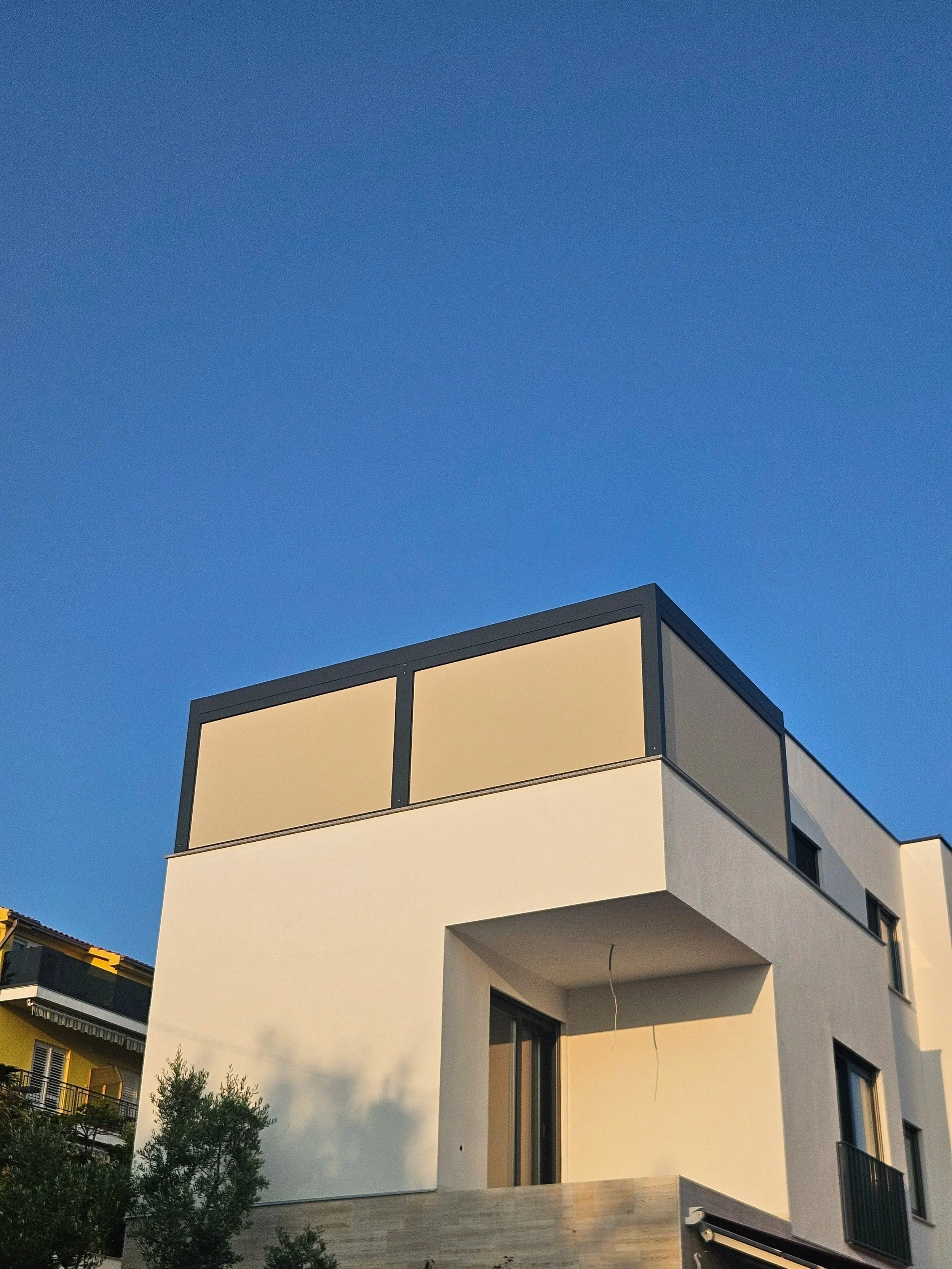 Modern white multi-story house with dark trim and balconies under a clear blue sky
