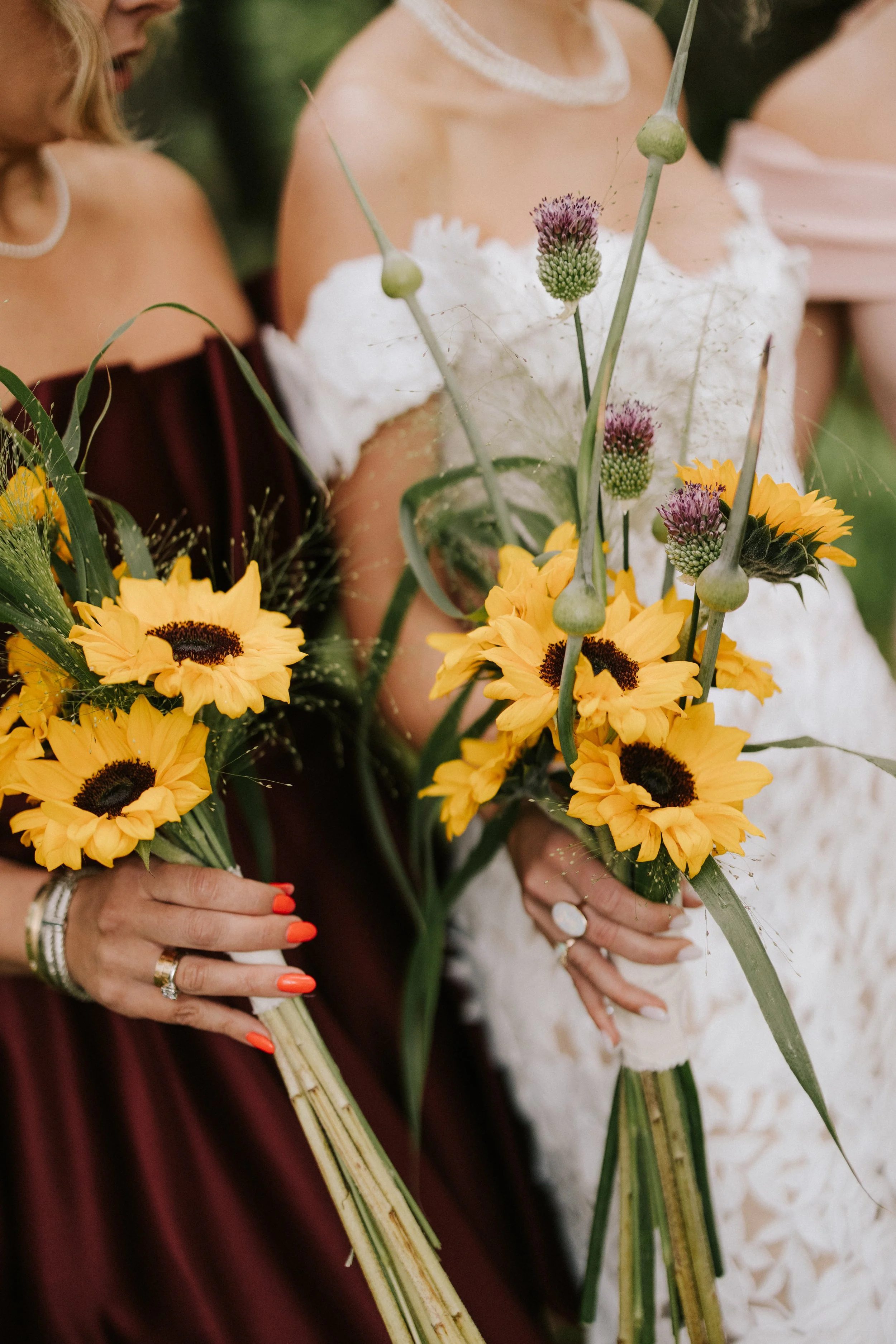 Two women in wedding dresses holding bouquets of sunflowers and wildflowers.