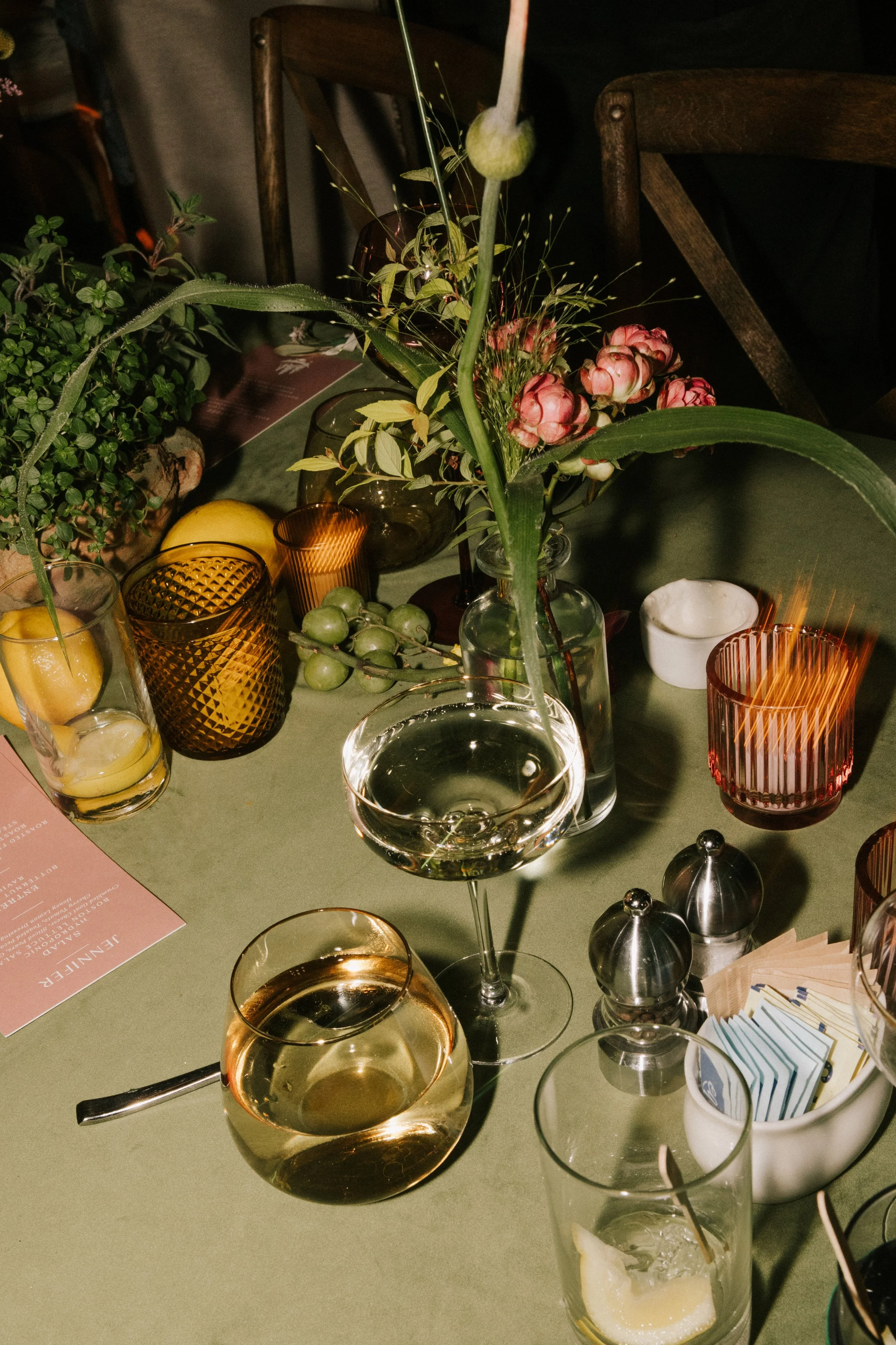 A table setting with glassware, a vase with pink flowers, napkins, salt and pepper shakers, and lemons.