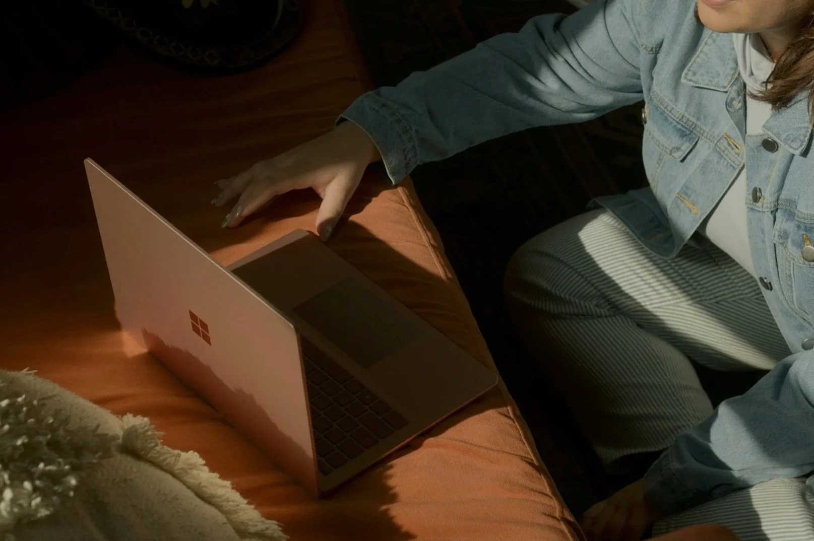 A person wearing a denim jacket and striped pants is sitting at a table while using a laptop.