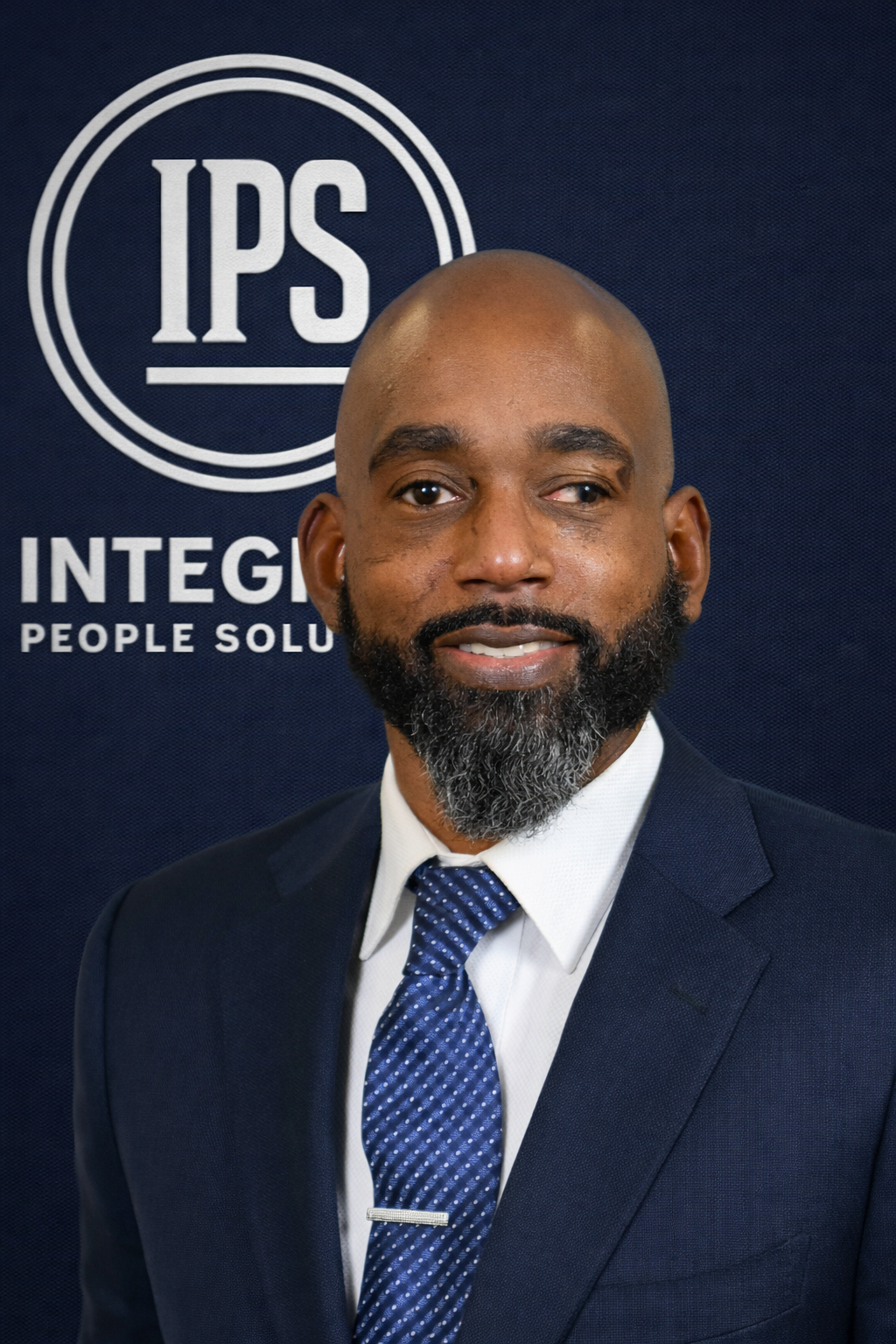 A man in a suit and tie smiling in front of a backdrop with the IPS logo and the words 'INTEGR' and 'PEOPLE SOLU'.