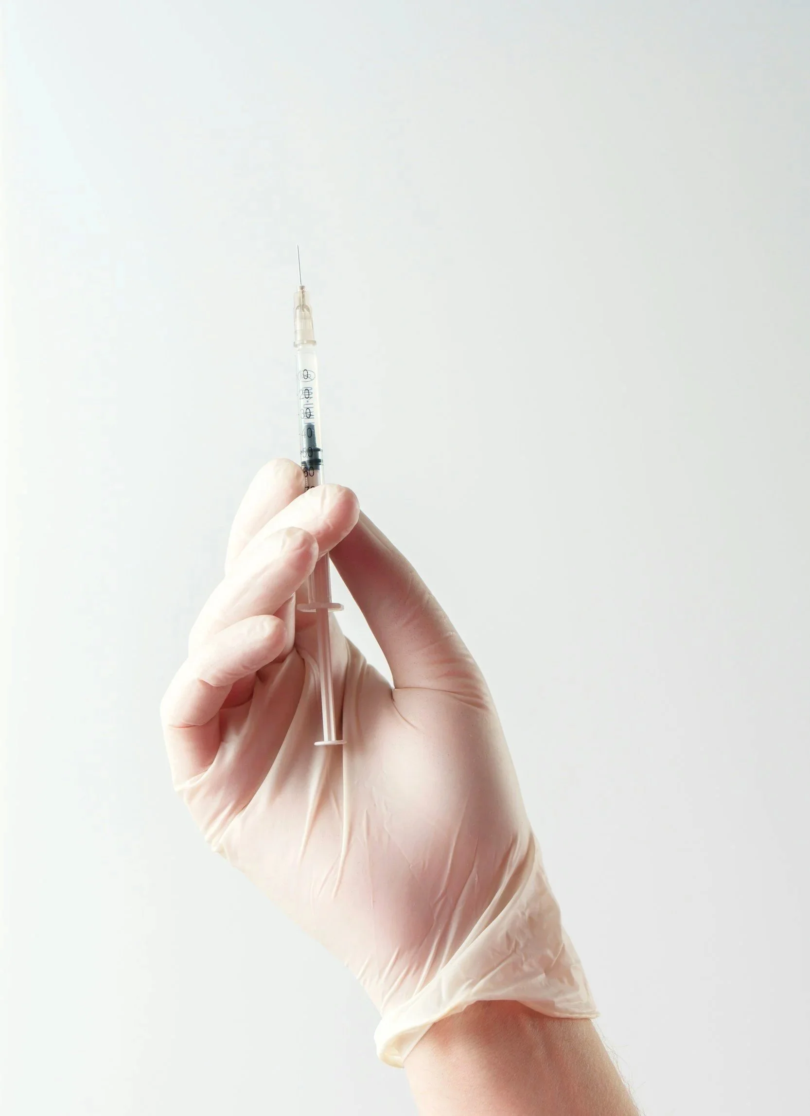 A hand with a glove holding a syringe against a white background.