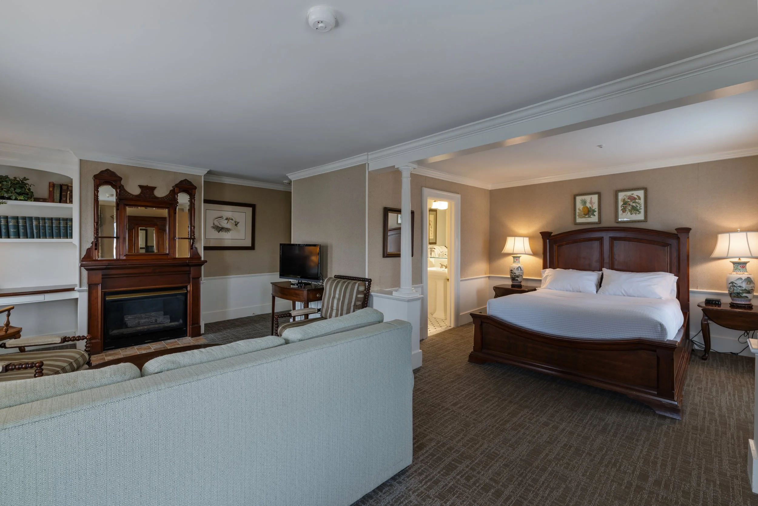 Interior of a hotel room with a bed, bedside lamps, framed artwork, a dresser, TV, and seating area.