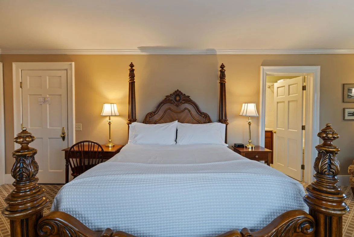 A bedroom with a wooden four-poster bed, two nightstands with lamps, and two closed doors.