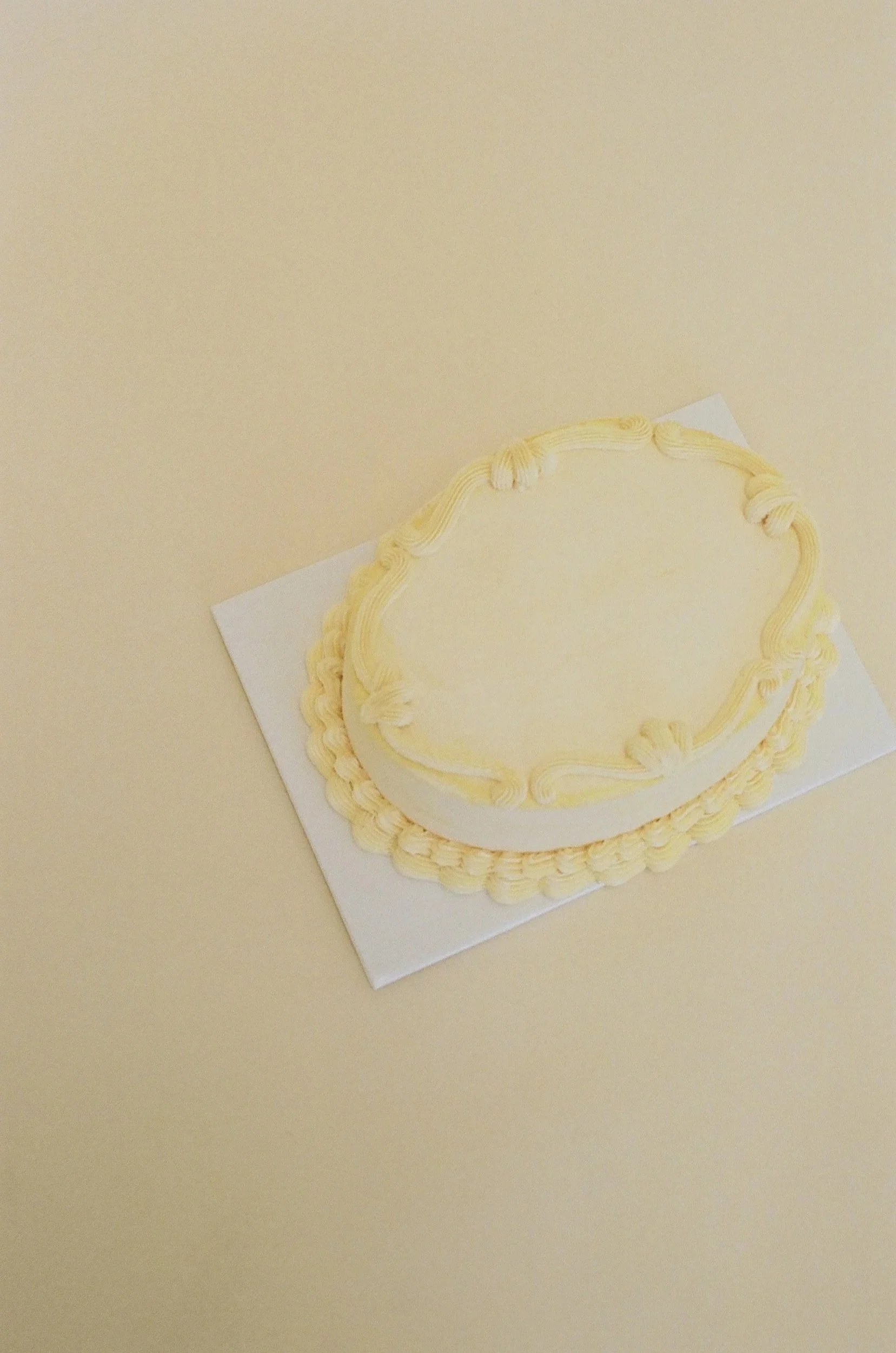 A cream cake with cream frosting piping decoration on top, placed on a white square base.