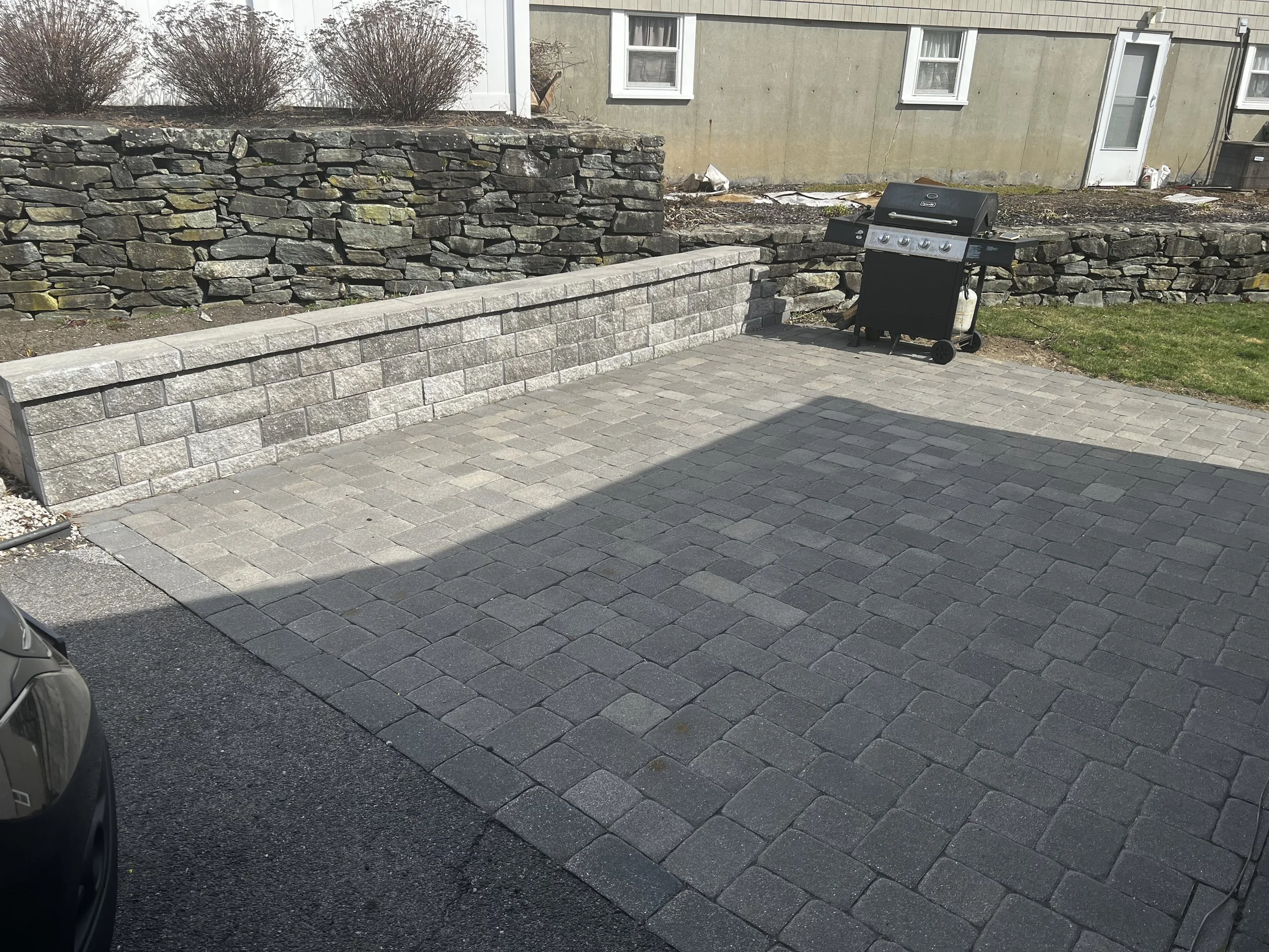 Custom paver patio and stone retaining wall installation in Metrowest Boston backyard with outdoor grill area. (Hudson, MA)