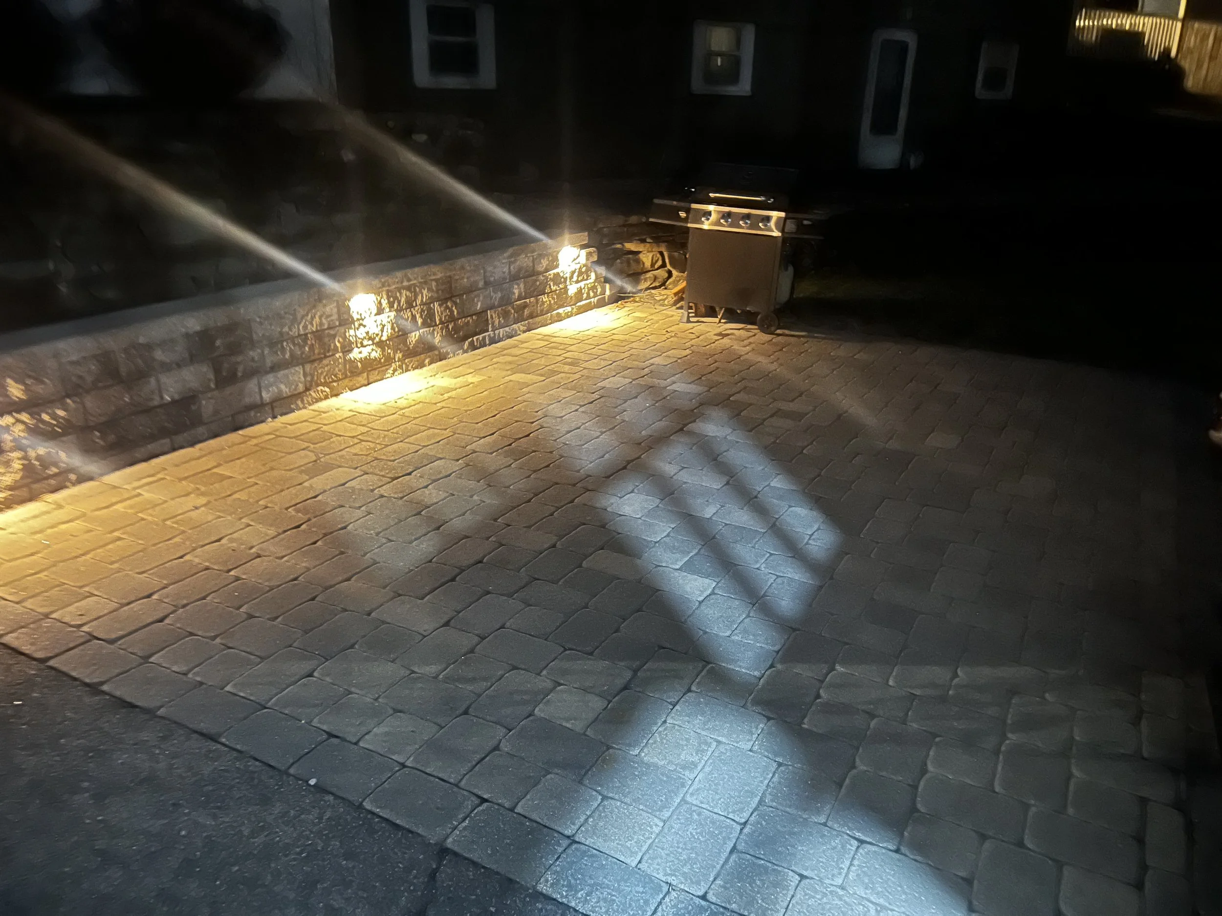 Outdoor patio lighting installation with brick pavers and stone wall in Metrowest Boston residential backyard. (Hudson, MA)