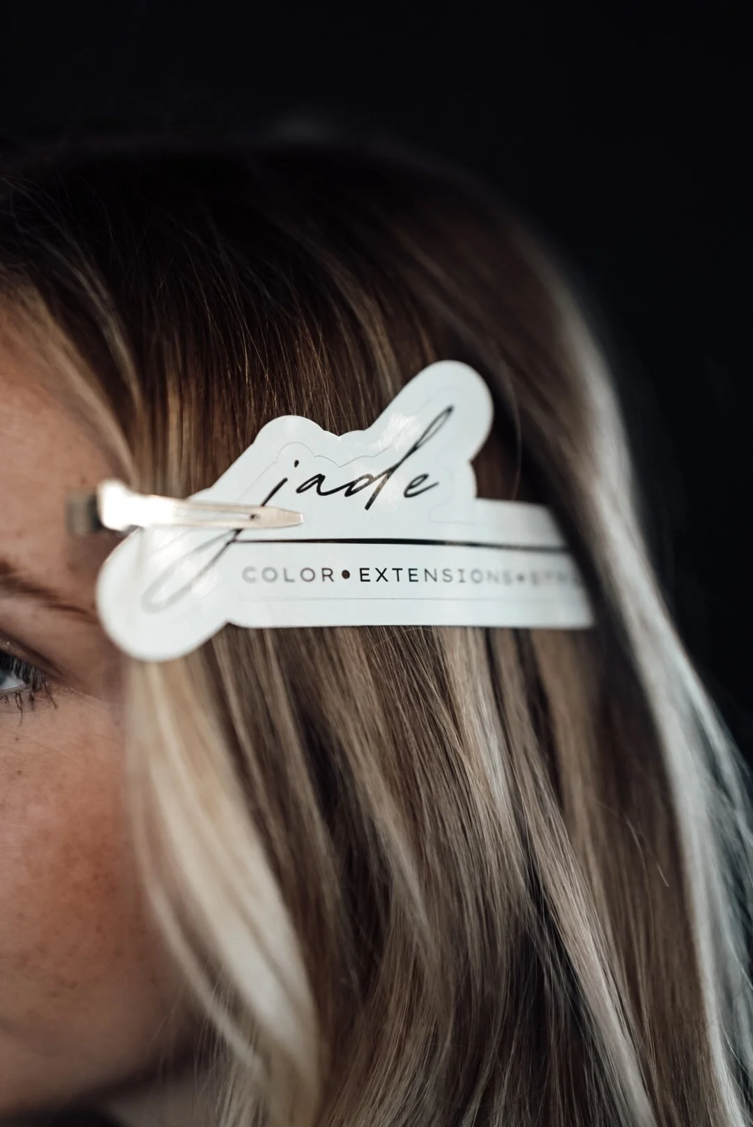Close-up of a section of a person's hair with a hair extension sample clipped onto it. The sample reads 'jade' and mentions color and extension details.
