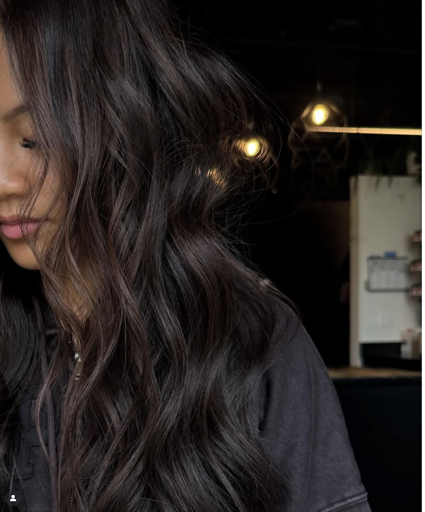 Close-up of a woman's dark brown hair with soft waves, partially covering her face in a softly lit indoor setting.