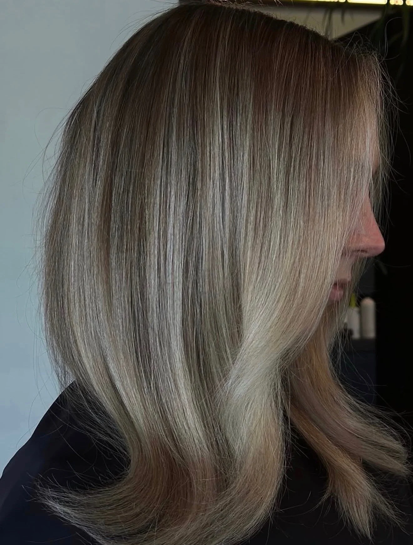 Close-up of a woman's side profile with shiny, blonde hair styled straight and layered.