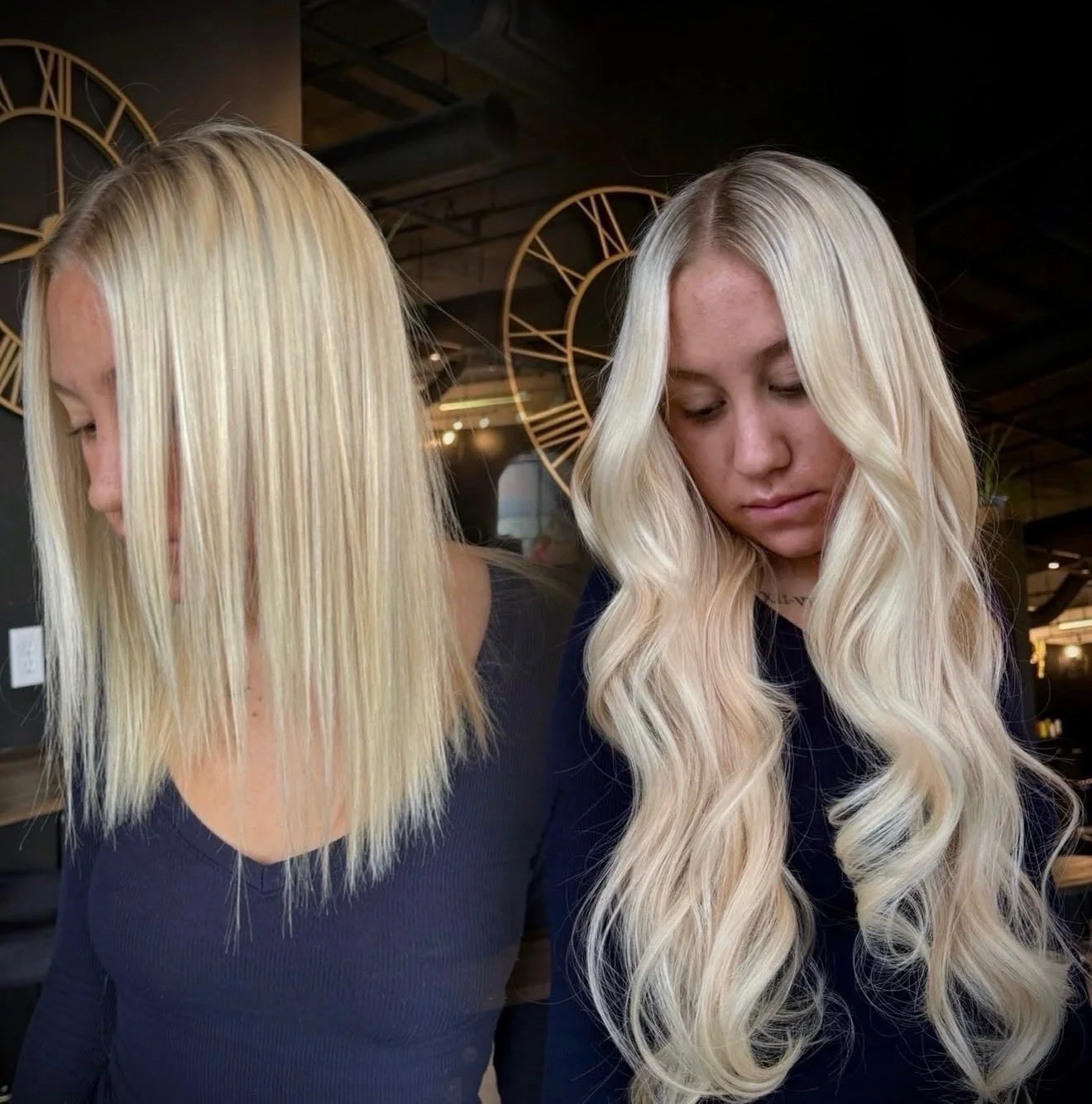 Two women with long blonde hair, one with straight hair and the other with wavy hair, in a modern indoor setting with clock decor in the background.
