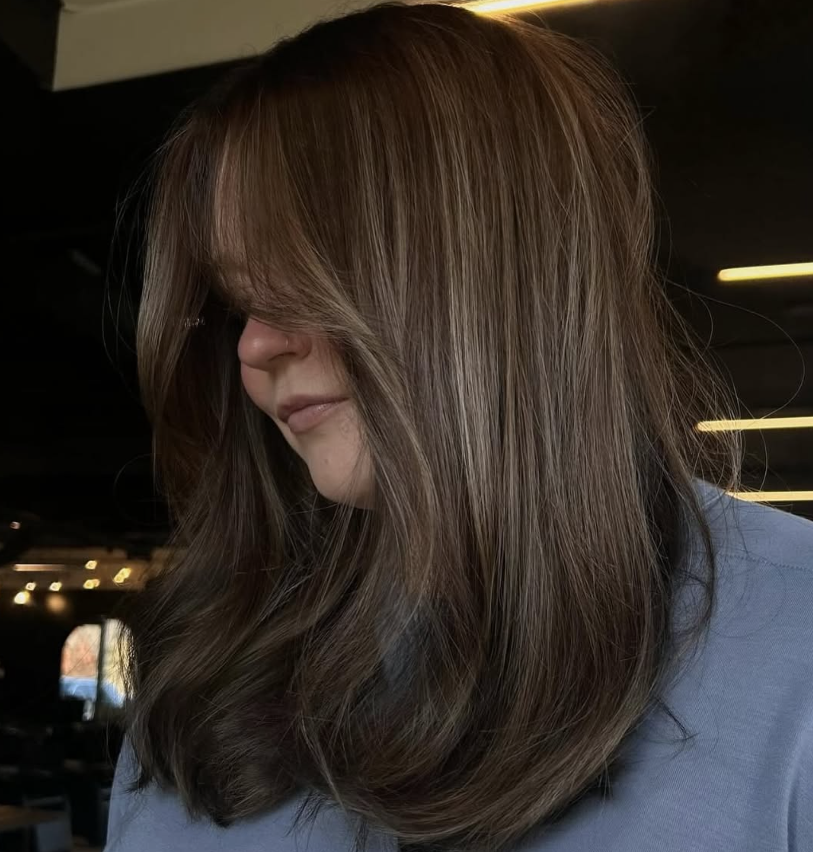 Close-up of a woman with long brown hair covering part of her face in an indoor setting.