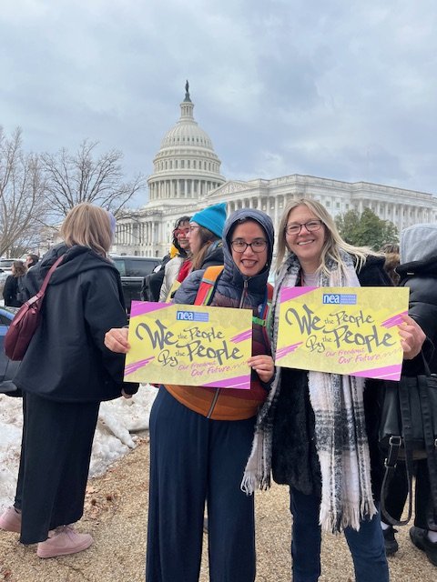 Two women protesting outside the U.S. Capitol building, holding signs that say "We the People, for the People, by the People" with a NEA logo. One of these women is Shannon Gibney, who is running for Minneapolis School Board in District 3.