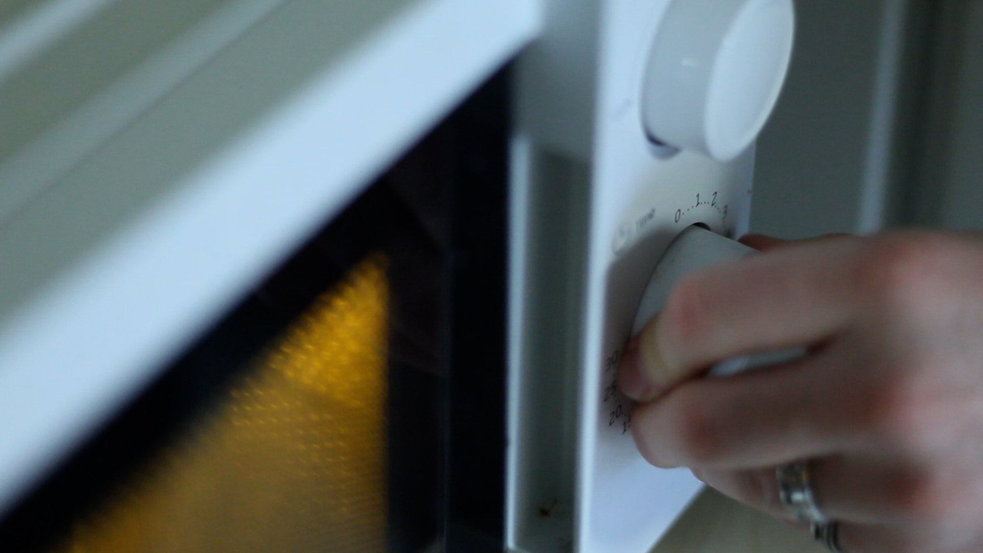 Close-up of a person's hand turning a dial on a kitchen microwave oven.