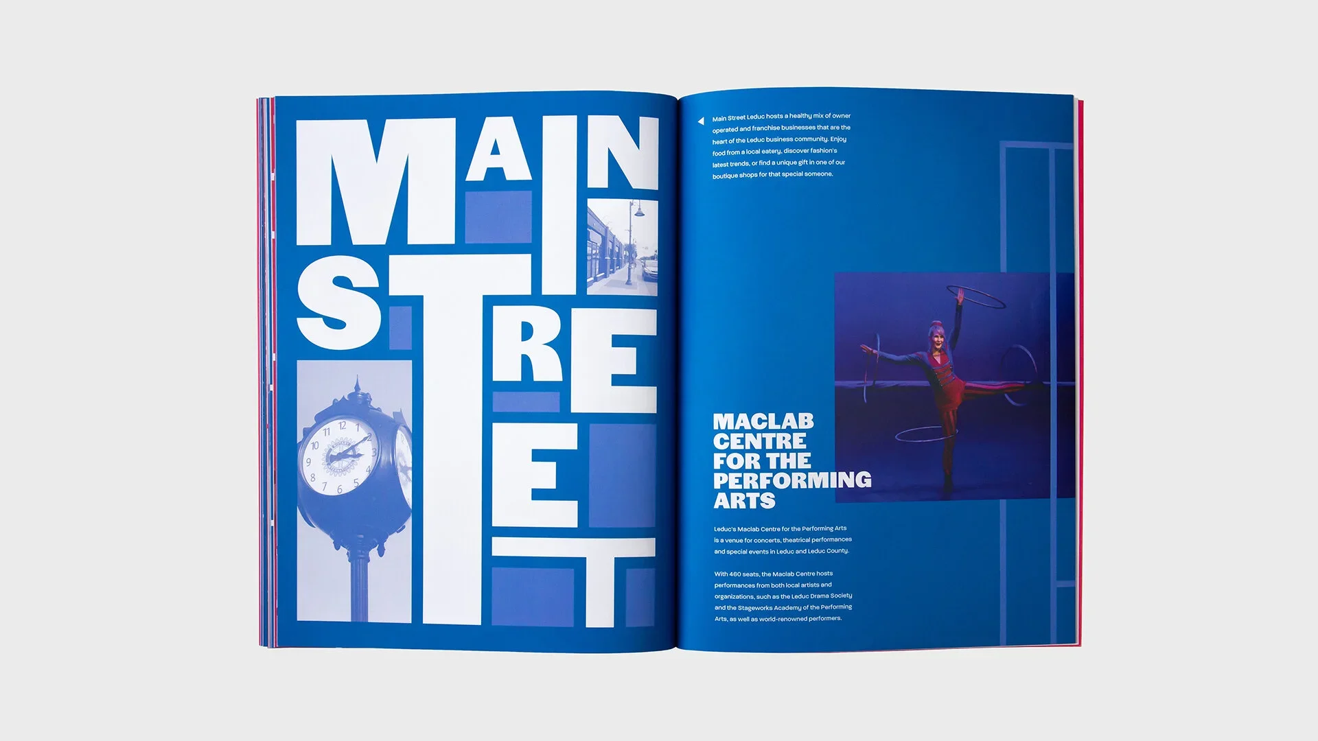 Open magazine showing a two-page spread with large, bold white text spelling "MAIN STREET" on the left page and a paragraph of small text along with a photograph of a performer with hoops on the right page.
