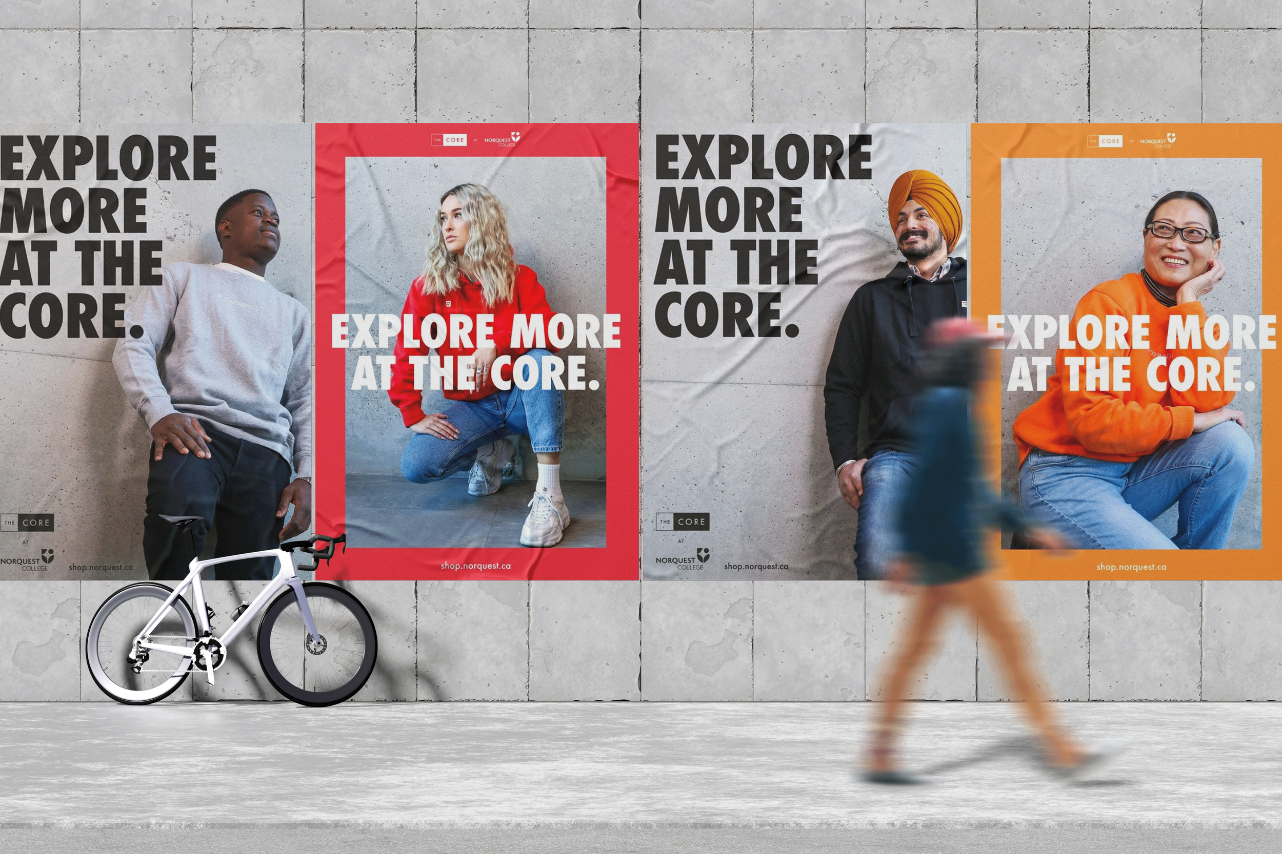 Three posters on a concrete wall featuring diverse people and the text 'Explore More at the Core.' a white bicycle leaning against the wall and a blurred person walking past.