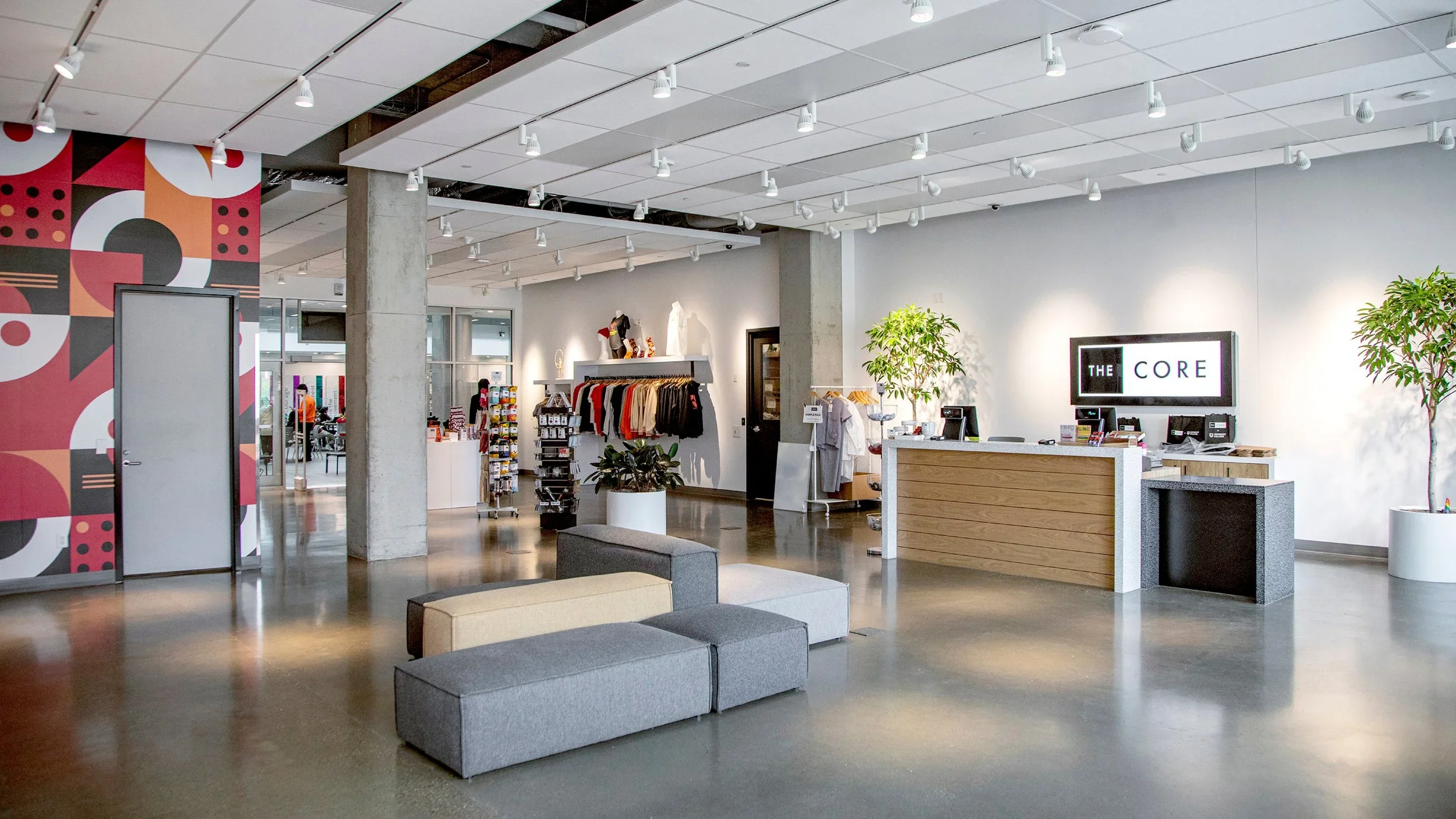 Interior of a modern retail store with a seating area, clothing display, checkout counter, and decorative plants.