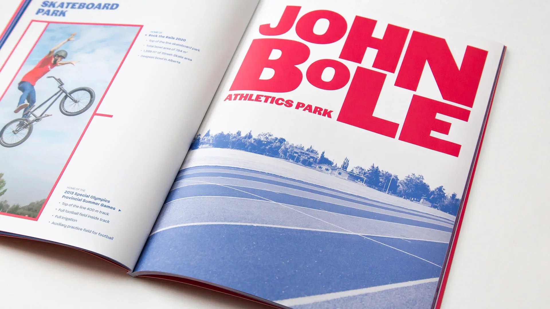 Open magazine showing a page with a large red text reading 'JOHN BOLLE ATHLETICS PARK' and a blue-tinted photo of an outdoor running track with trees and buildings in the background.