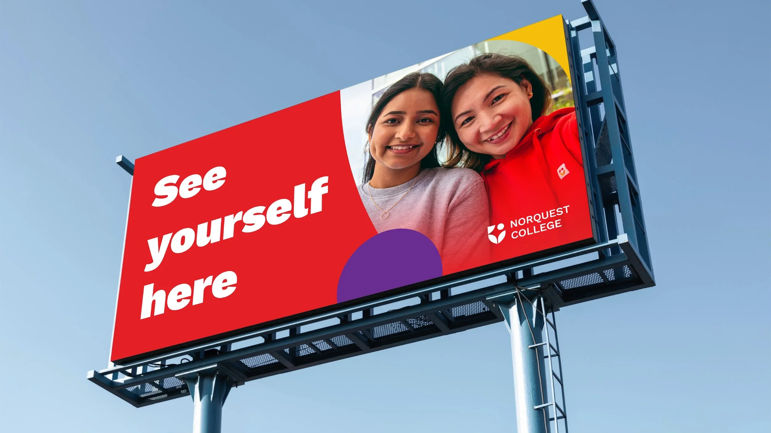 A billboard with a red background featuring two smiling women, one wearing a gray shirt and the other in red, promotional message 'See yourself here,' and the Norquest College logo.