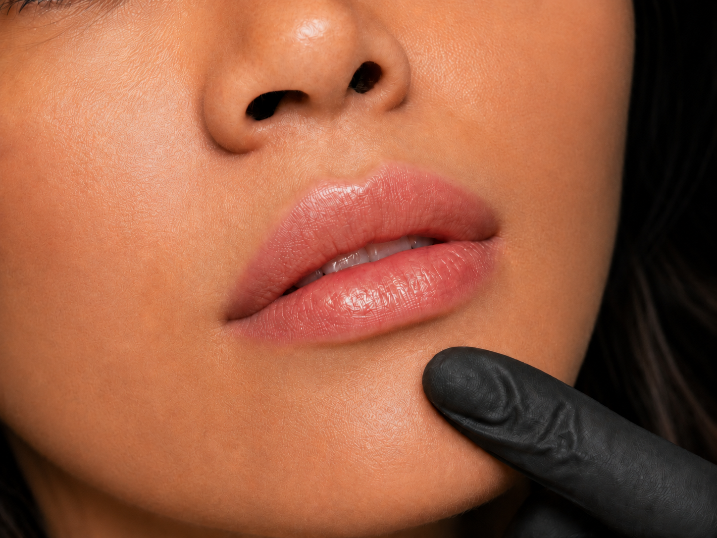 Close-up of a woman's face showing her nose and lips, with a gloved finger touching her chin.